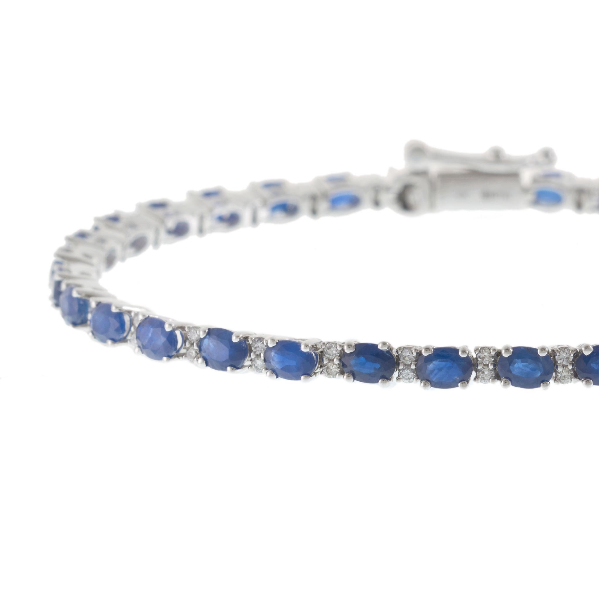 Questo bracciale tennis in oro bianco 14KT è una raffinata dimostrazione di colore e maestria, con un'alternanza di zaffiri blu a taglio ovale e diamanti rotondi a taglio brillante, ognuno dei quali incastonato meticolosamente per creare un flusso