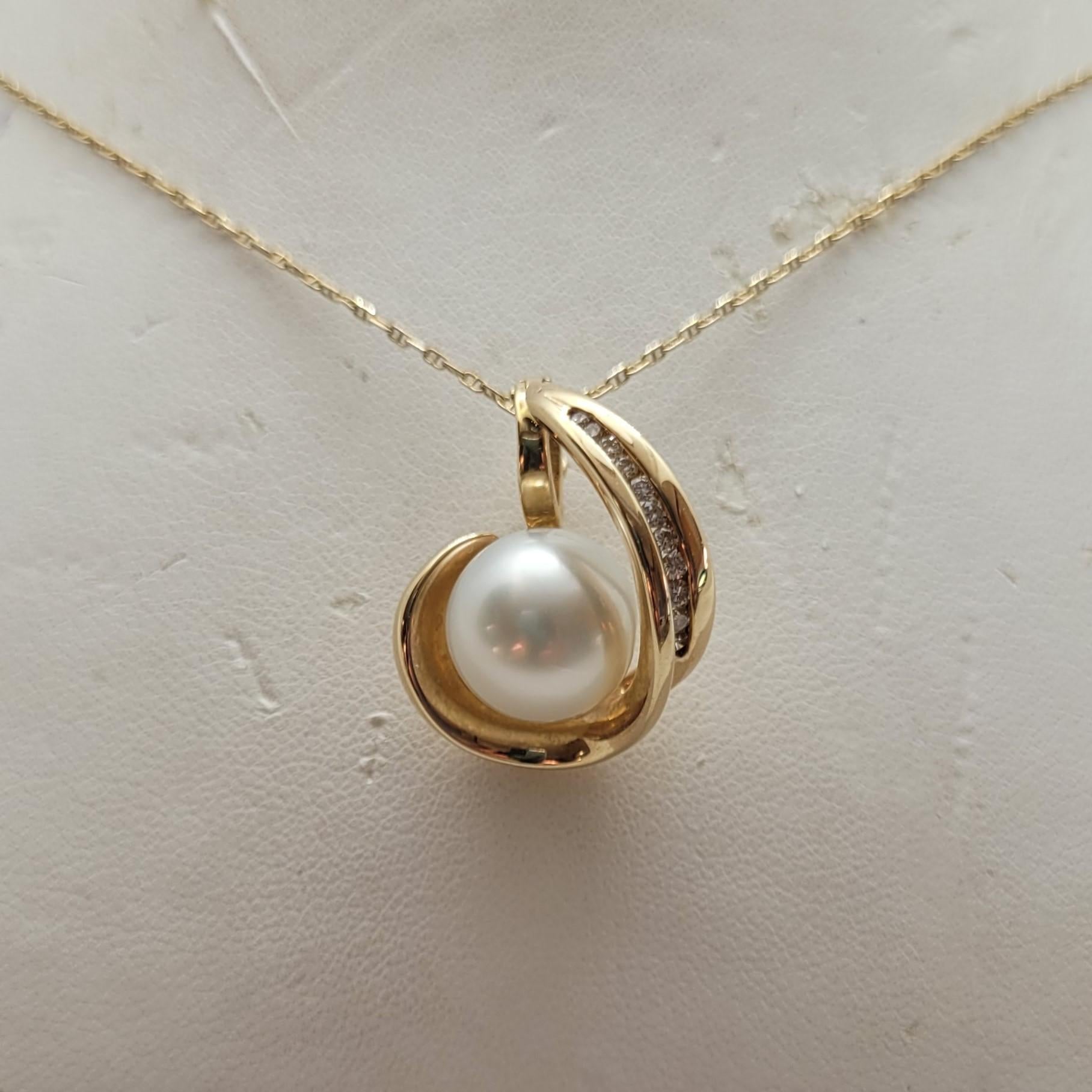 Ce magnifique pendentif est en or jaune 14kt et présente une perle de culture blanche de 11 mm entourée de 11 diamants ronds de taille brillant, totalisant environ 0,15 carats. La perle présente une belle couleur blanc gris moyen lustrée,