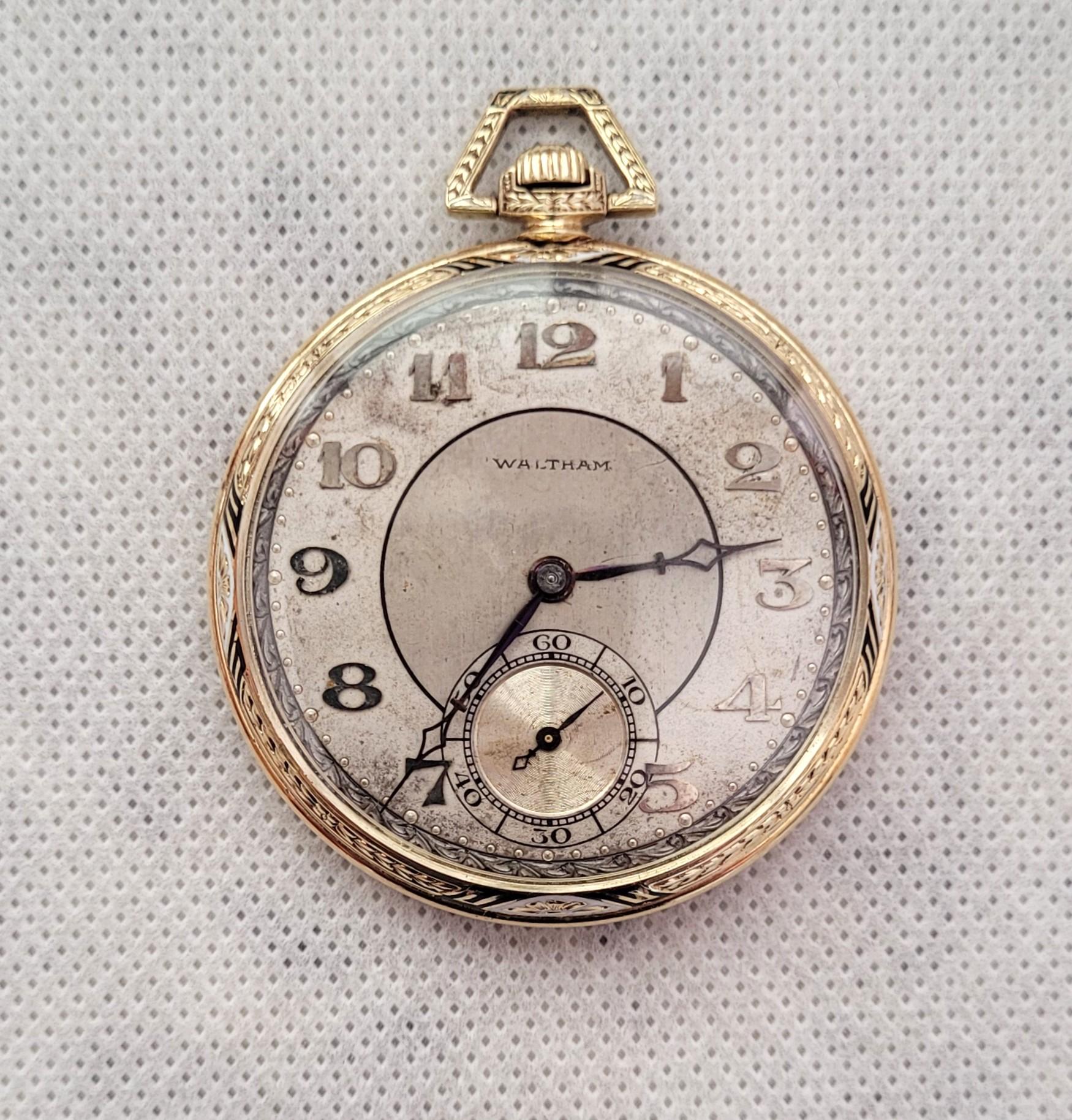 Ti presentiamo uno splendido orologio da tasca Waltham del 1923 in oro giallo 14kt, con cassa da 44 mm impreziosita da squisite incisioni e da un sorprendente disegno di foglie in smalto bianco e nero. Questo straordinario segnatempo è stato