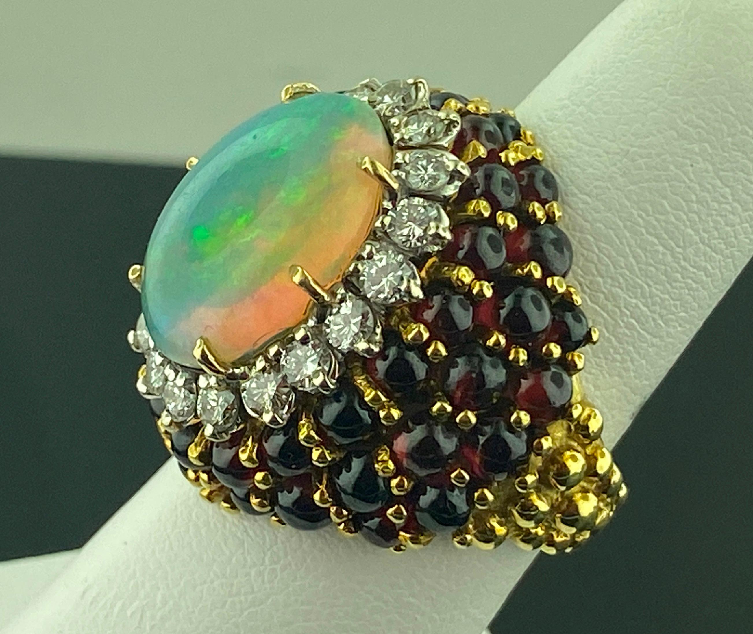 Set in 14 karat yellow gold, weighing 23 grams, is a 7 carat Oval Cut Cabochon Opal with 18 Round Brilliant Cut diamonds weighing 1.25 carats, Color Grade of: G-H, Clarity Grade of: VS plus numerous Garnet beads.  Ring size is 8.25.