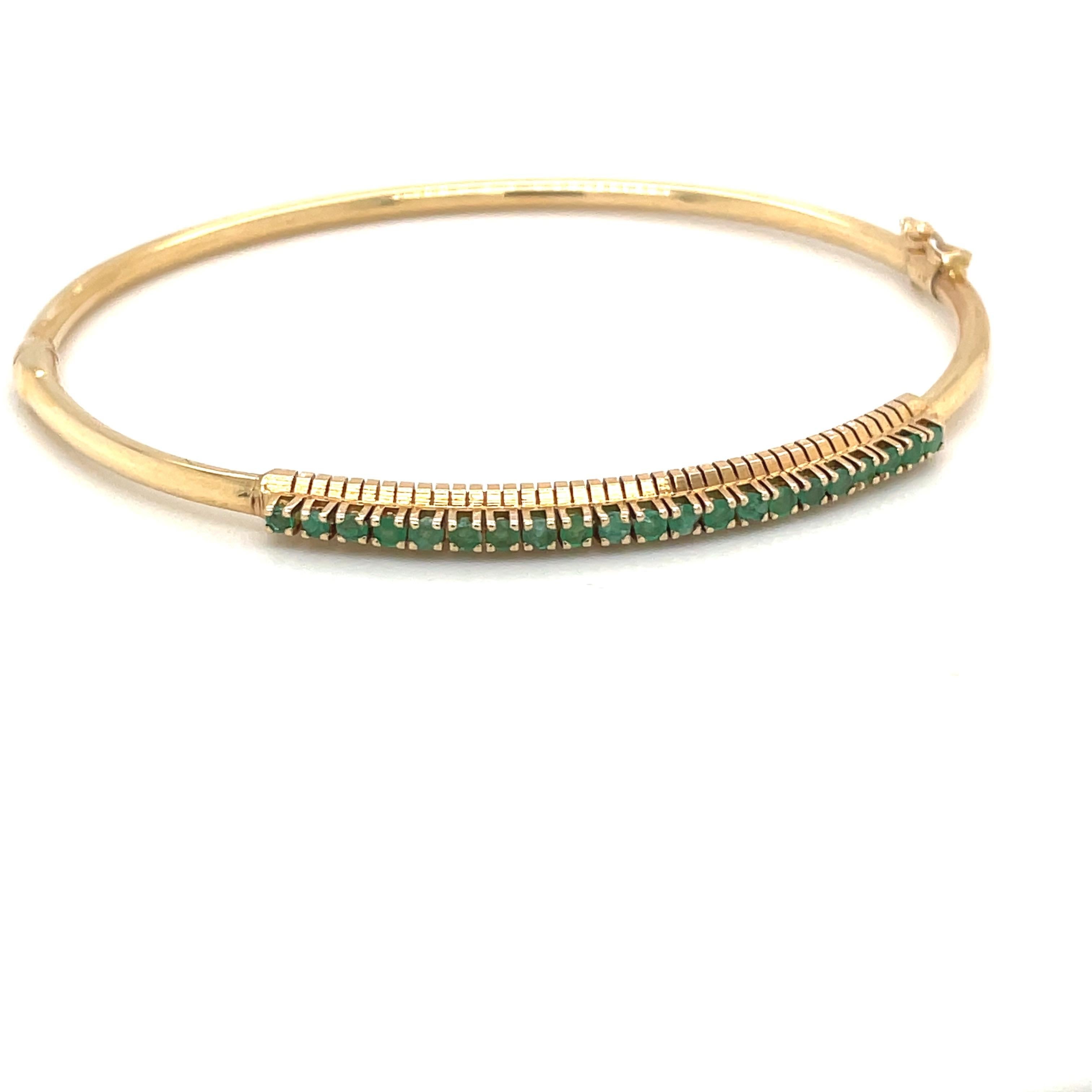 A 14 karat yellow gold bangle bracelet with a single row of prong set  round emeralds. The hinged bracelet measures 2.5