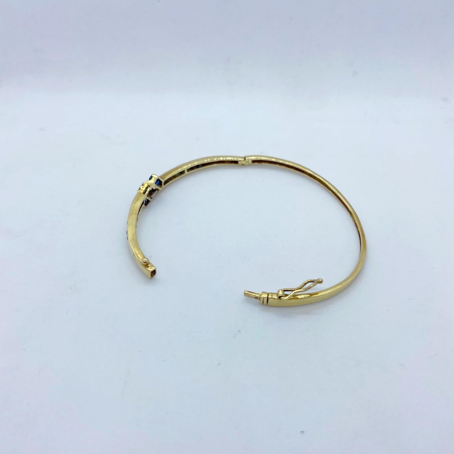 14 karat yellow gold bangle bracelet designed with 1.15 carats of round blue sapphires and 0.20 carats of round diamonds. The bracelet measures 2.5
