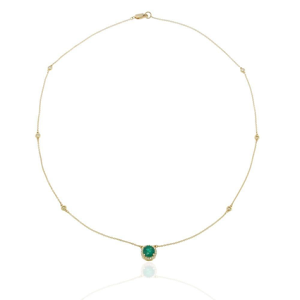 A graceful 14KT yellow gold necklace featuring a vivid round emerald centerpiece surrounded by a sparkling diamond halo. Accented with bezel-set diamond stations throughout the fine gold chain, this delicate design balances luxury with a minimal