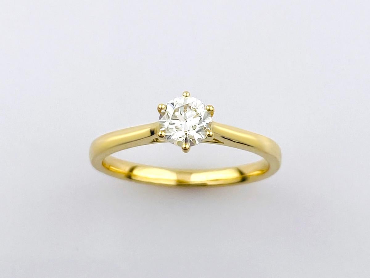 Cette bague solitaire classique présente un design intemporel et élégant, idéal pour une bague de fiançailles ou un cadeau important. Elle est ornée d'un seul diamant brillant de taille ronde, solidement maintenu dans une monture à six griffes de