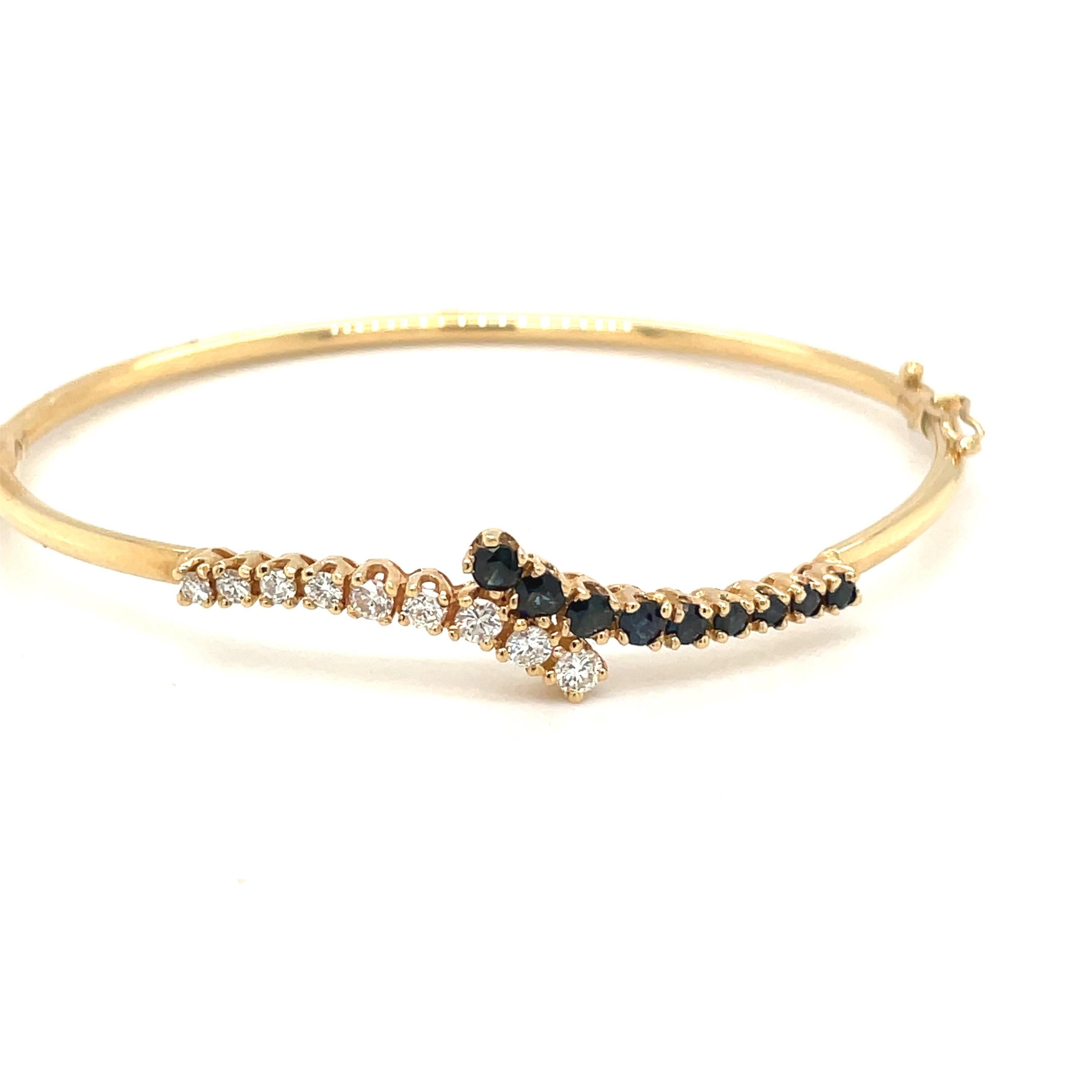 14 karat yellow gold bangle bracelet set with a single row of round diamonds and a single row of blue sapphires. The hinged bracelet measures 2.5