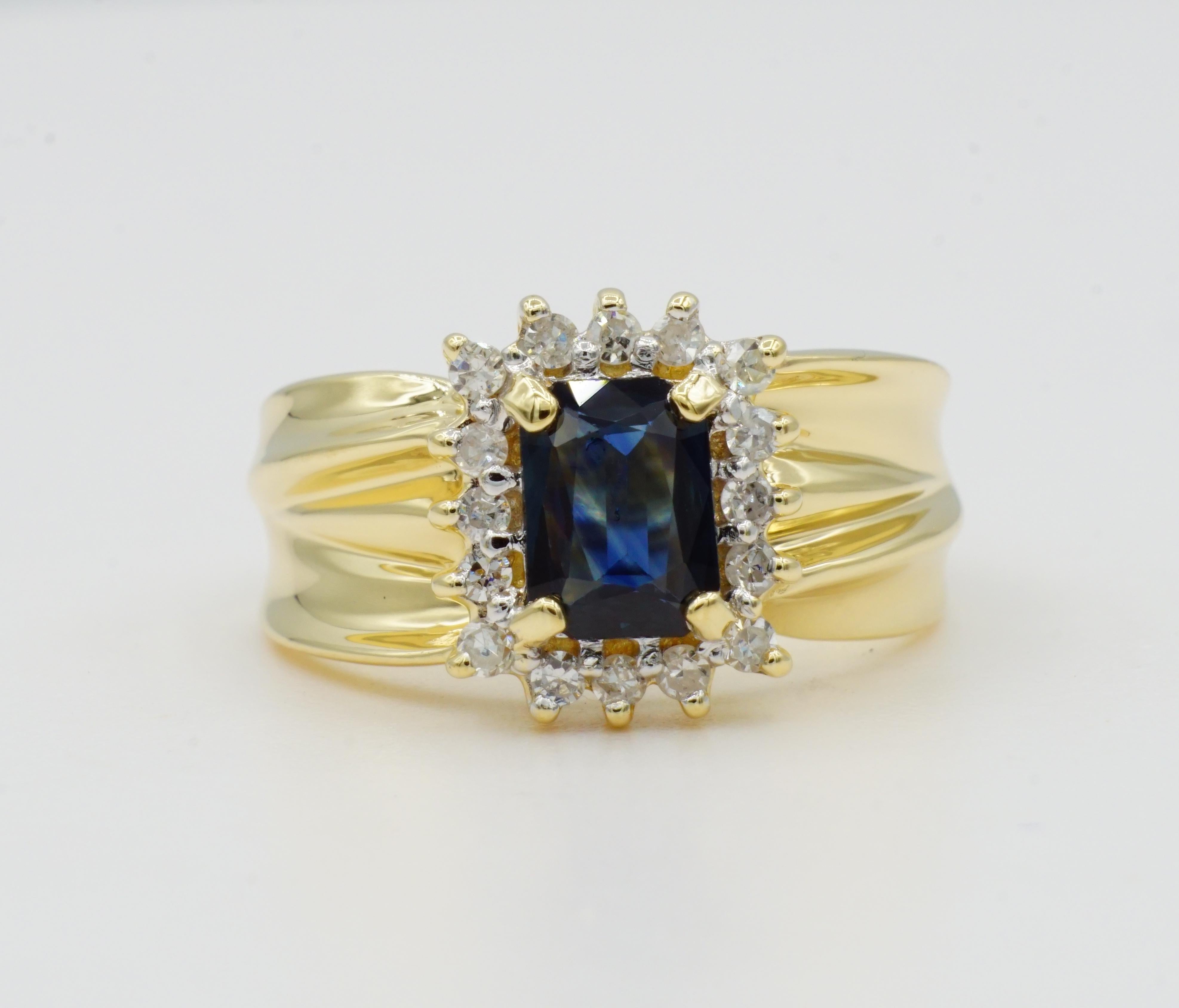 14kt yellow gold ring with a 5 x 7mm emerald cut sapphire (approximately 1.00ct) with rich medium blue color set in a four-prong style setting accented with 16 prong-set round single cut diamonds of .35cttw.  The diamonds are G/H in color and SI in