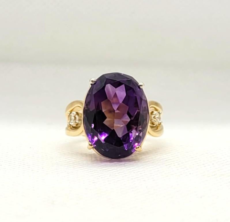Si tratta di un anello in oro giallo 14kt in stile cattedrale con un'ametista dal taglio ovale di 18mm x 14mm. L'ametista è saldamente incastonata in una montatura a cesto a quattro punte ed è impreziosita da due diamanti tondi brillanti, per un