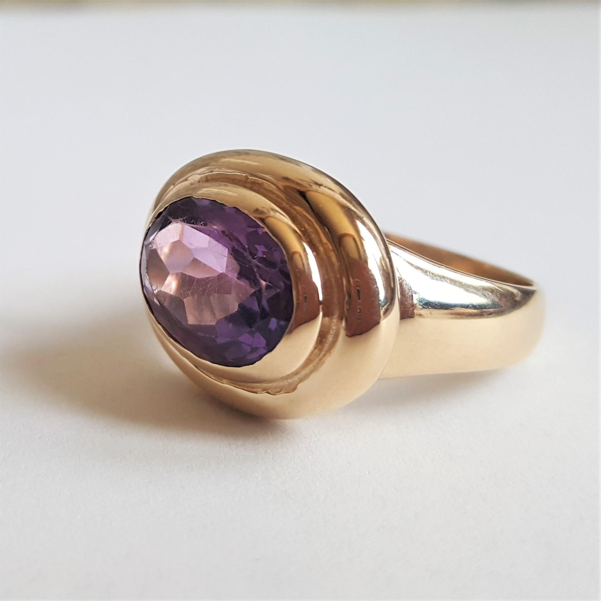 14kt yellow gold ring with a complete bezel set 14mm x 9mm oval purple amethyst set east-west. The ring is size 9, 12 grams in weight, 20mm x 16mm at the top and the shank is 9mm tapering to 4mm. The purple amethyst has a rich color and is slightly