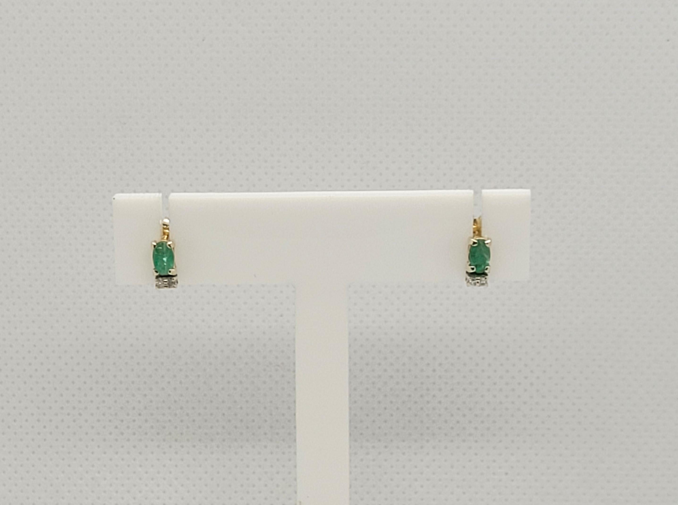 14kt yellow gold friction post earrings with two oblong oval emerald gemstones, and four round single-cut diamonds. The 4.8 x 3mm emerald and 1.2mm diamonds are commercial grade (fair-quality with visible inclusions), I clarity, and K color. The