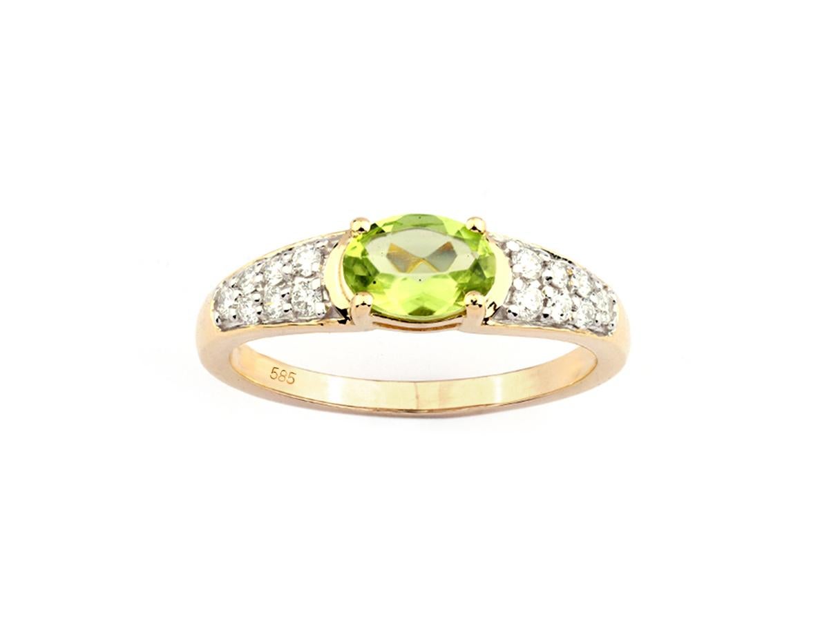 El anillo tiene un diseño clásico y elegante. Un prominente peridoto de talla oval está engastado en el centro. Los hombros de la banda están engastados con múltiples diamantes blancos pequeños y redondos que descienden por la banda, añadiendo un