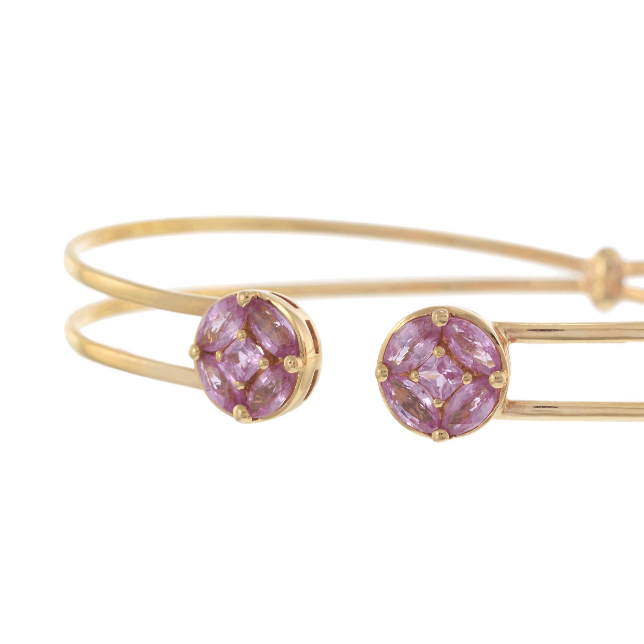Este elegante brazalete abierto de oro amarillo de 14 quilates presenta dos engarces circulares en racimo, cada uno adornado con vibrantes zafiros rosas que suman aproximadamente 1,71 quilates. El delicado diseño de doble banda ofrece una sensación