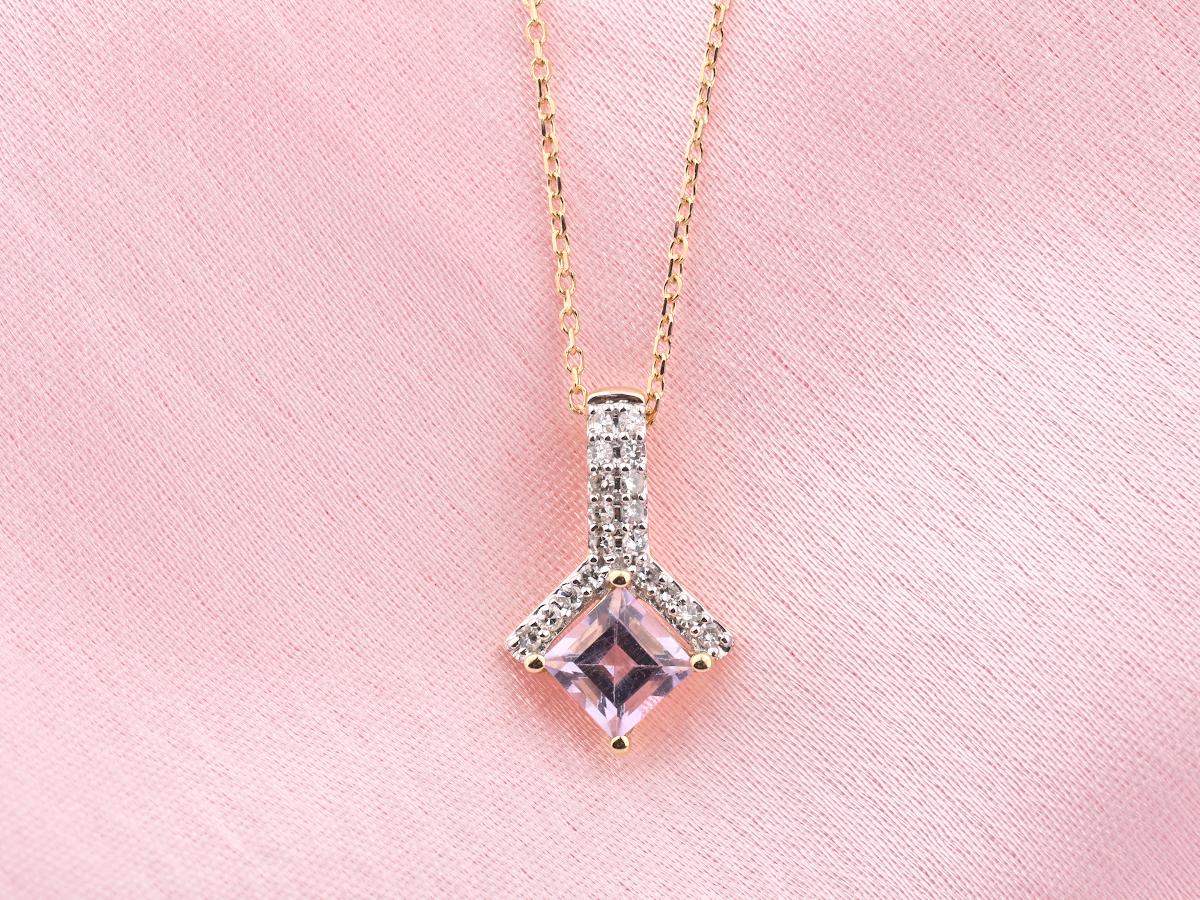 El colgante presenta un diseño de gota moderno y elegante. Una amatista cuadrada o talla princesa está engastada en la parte inferior, sujeta por puntas de oro. Encima de la amatista hay una sección en forma de V o cruzada engastada con pequeños