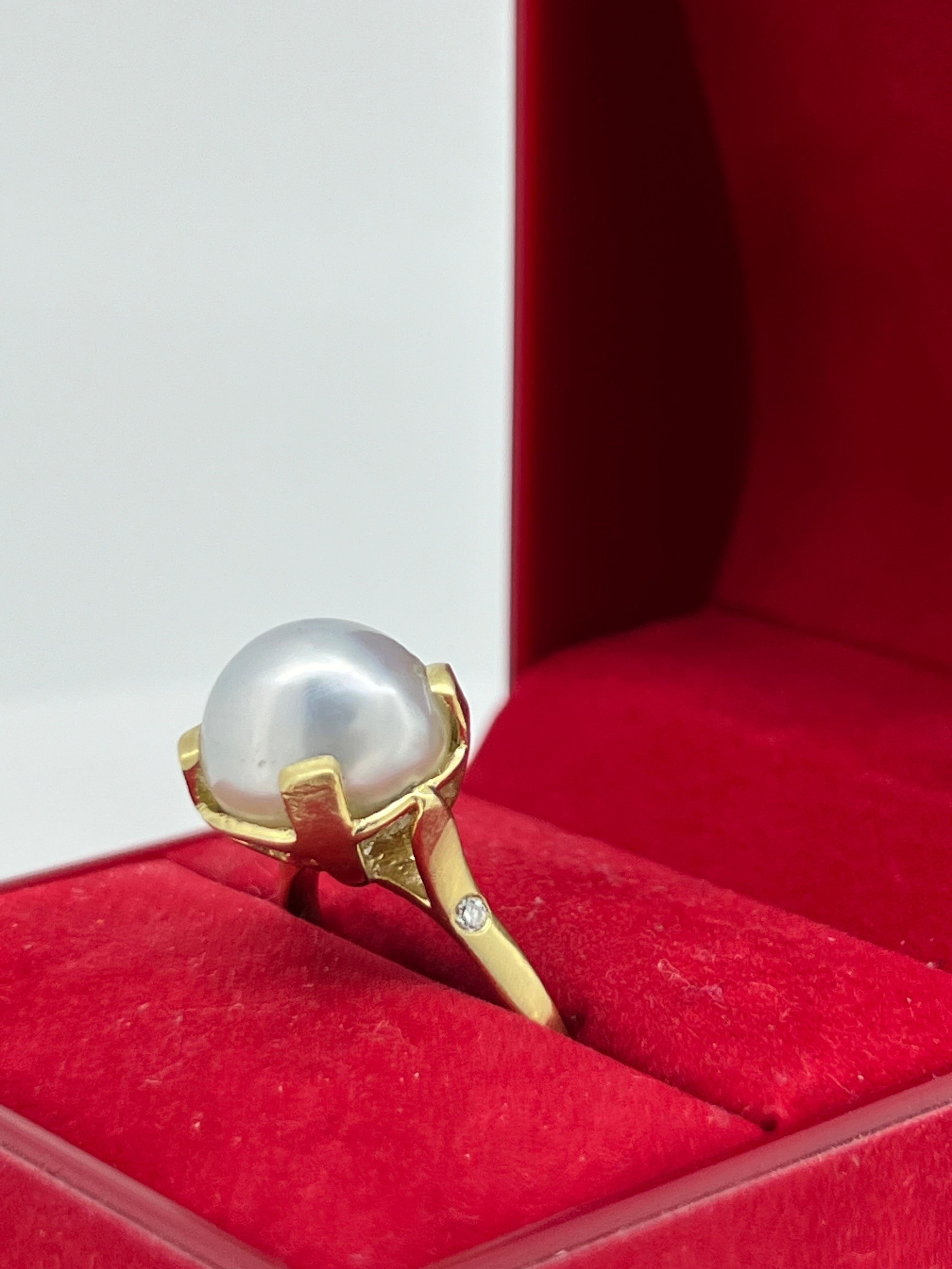 Sorgfältig aus 18 Karat Weißgold gefertigt, 
Dieser Vintage-Ring ist in der Mitte mit 4 Krallen besetzt und mit einem 
Runde Perle von beeindruckenden 14mm 
von feiner cremefarbener Elfenbeinfarbe und spiegelglänzend,

in einer Fassung aus 18K