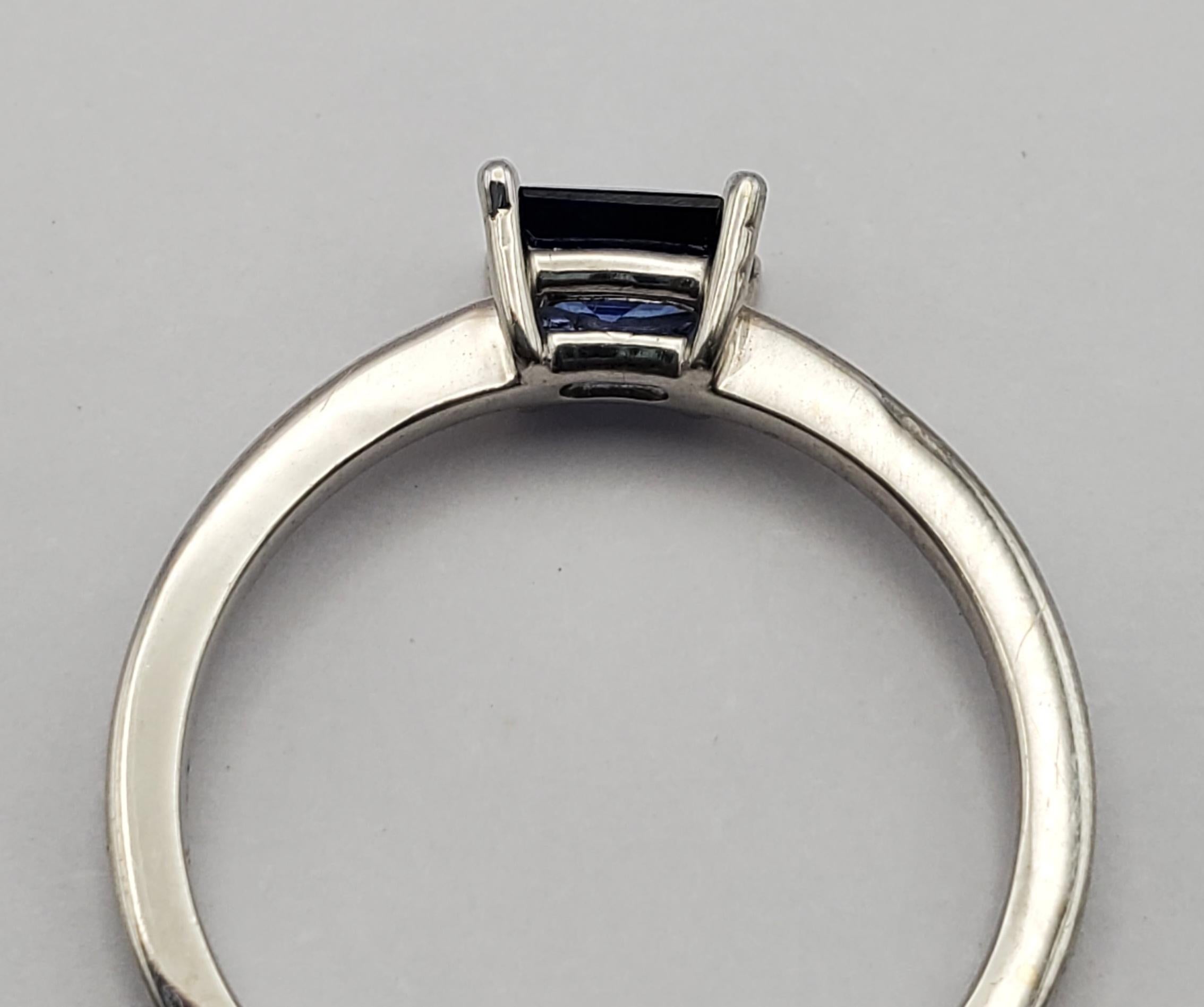 Beautiful natural blue sapphire east/west solitaire ring. This ring features a vibrant blue, elongated radiant cut stone weighing 0.70ct set into a four prong basket setting. The ring is currently a size US size 7, but could be size by a jeweler to
