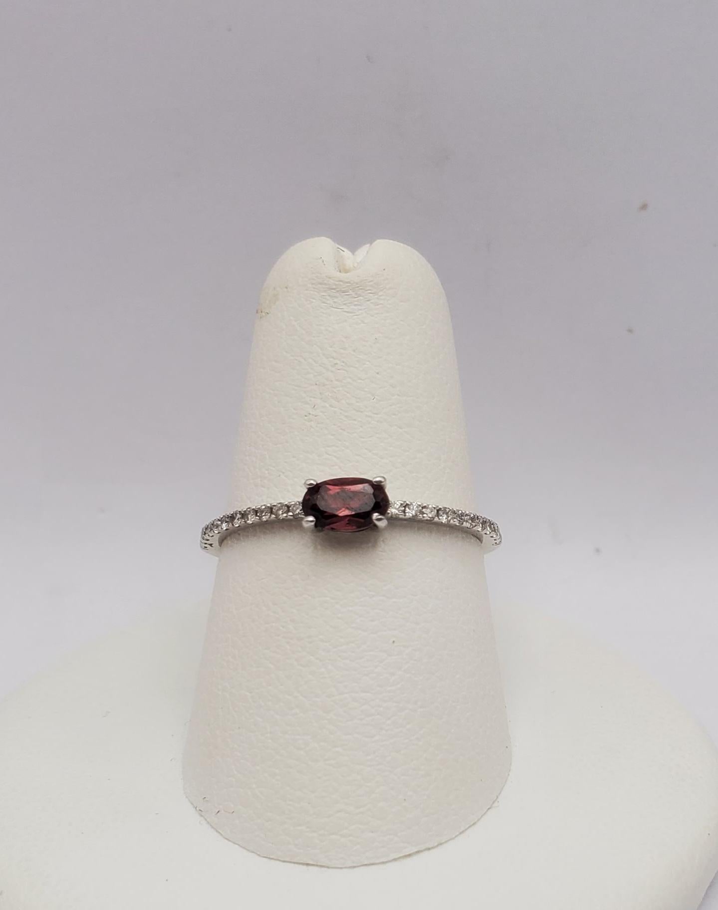Encantador anillo de oro blanco de 14k, granate y diamantes. El anillo presenta una piedra de granate de Mozambique de talla oval alargada engastada al este/oeste con un peso de 0,25cts y veintidós diamantes naturales redondos de talla brillante con
