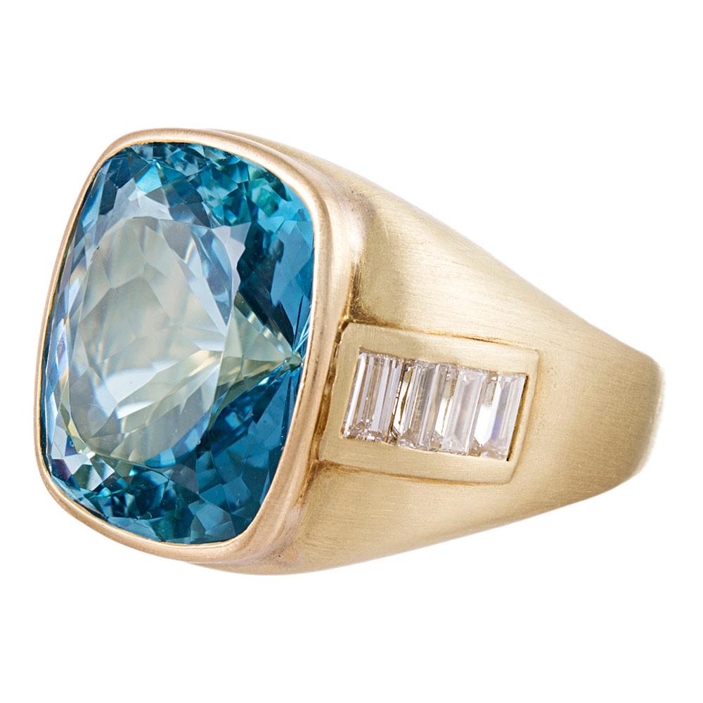 A setting of beautifully treated 18 karat yellow gold, with a subtly textured satin finish is set in the center with a cushion shaped aquamarine of 15 carats and accented with baguette diamonds on the shoulders. This piece possesses a softness,