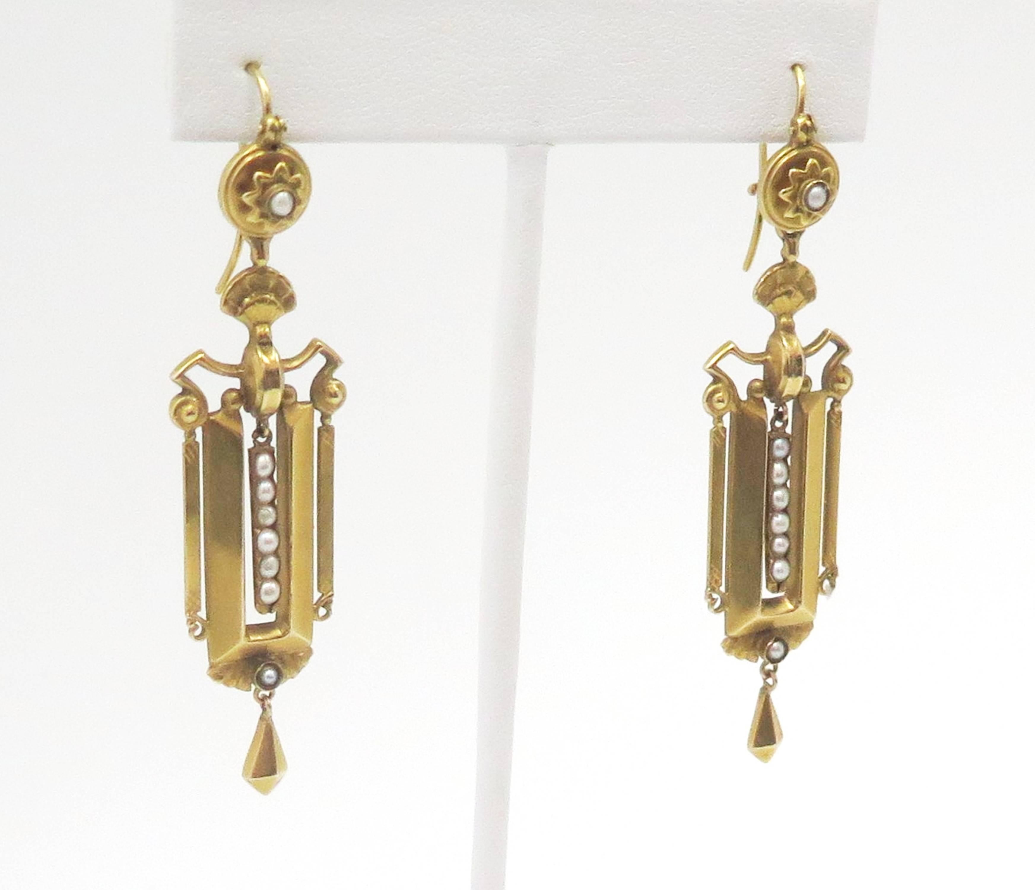 In rich 15K yellow gold, a unique and lovely pair of dangling earrings detailed with delicate pearls. The earrings are geometrically inspired yet softened with  lustrous seed pearls that shimmer down the middle. The center piece dangles gracefully