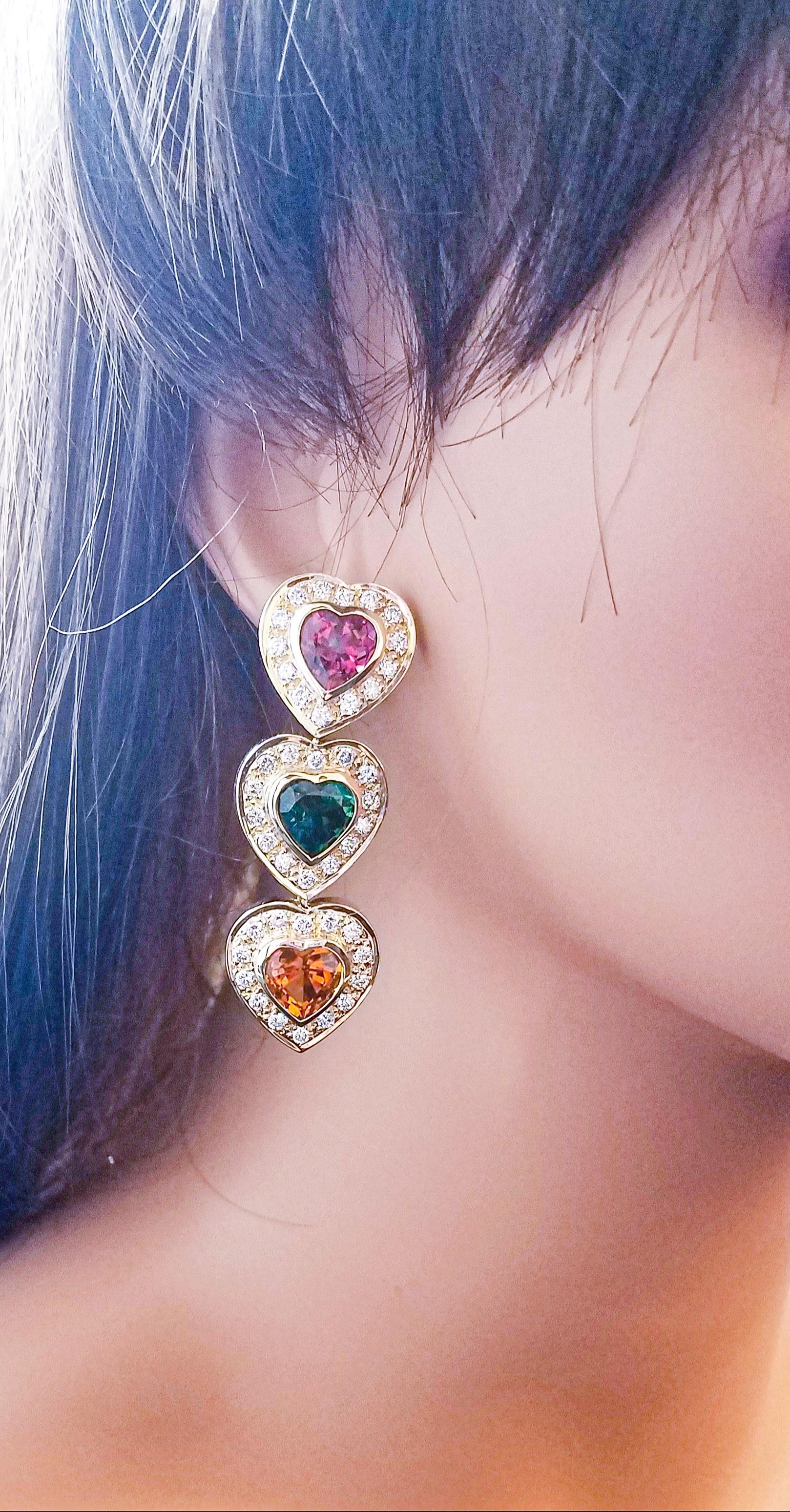 These heart cluster halo earrings are made in a brightly polished 14 k karat yellow gold finish and contain a total of 15.00 carats of vibrant multi-colored tourmaline heart-shaped stones prong-set in the center. These tourmalines exhibit a natural,