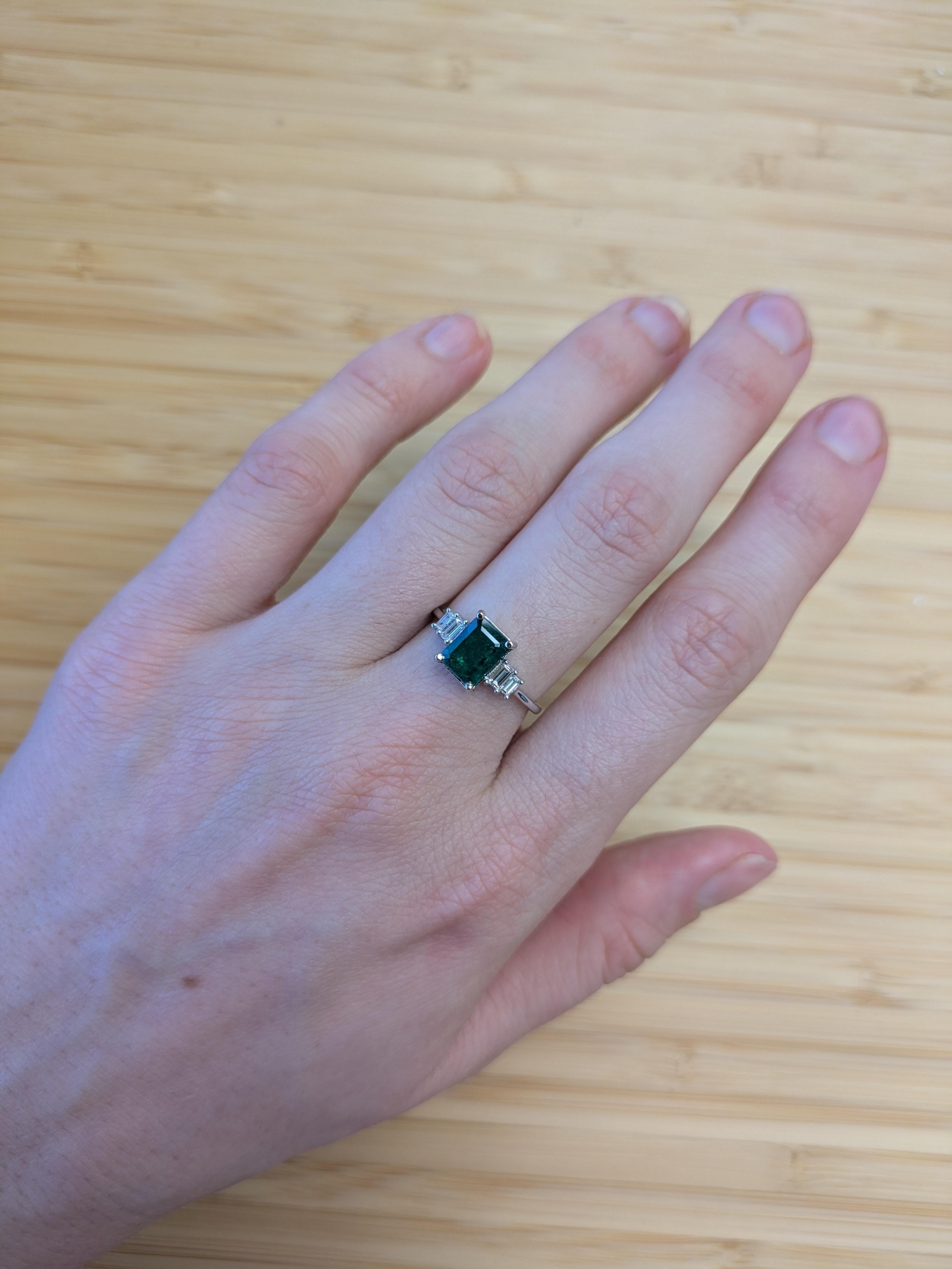 Dieser zeitlose Ring mit drei Steinen besteht aus einem 1,5 Karat schweren sambischen Smaragd, der von funkelnden Diamanten aus Erdminen flankiert wird. In massivem 14-karätigem Gold gefasst, ist er eine anmutige Mischung aus lebendiger Farbe und