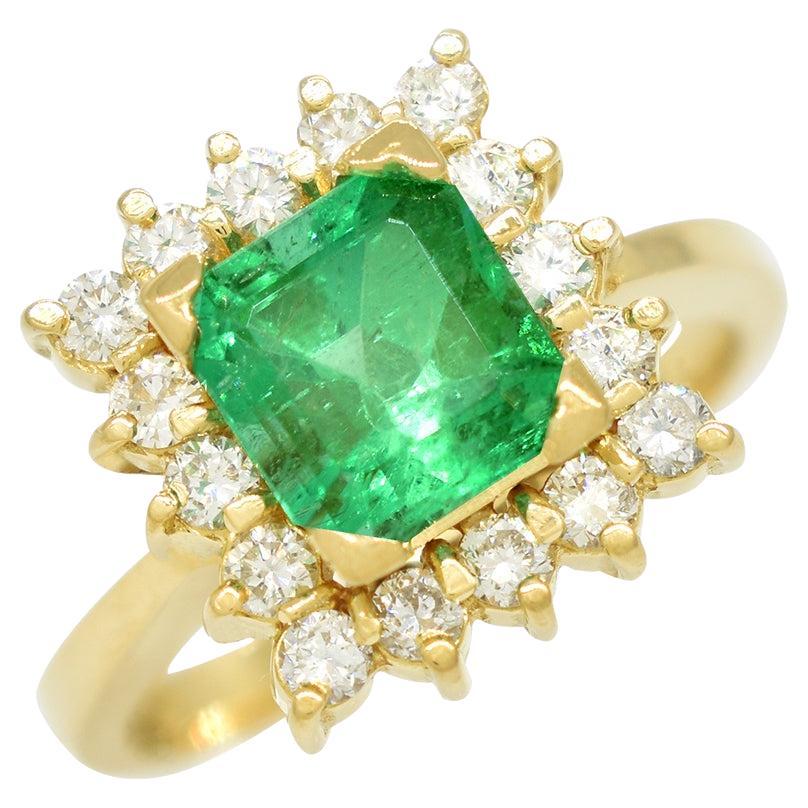 Emerald and diamond cocktail ring custom made in solid 18K gold for this stunning 1.50 Carats emerald cut natural emerald with a vibrant medium green color full of life. Surrounding the emerald are 16 round-cut diamonds, each carefully selected for