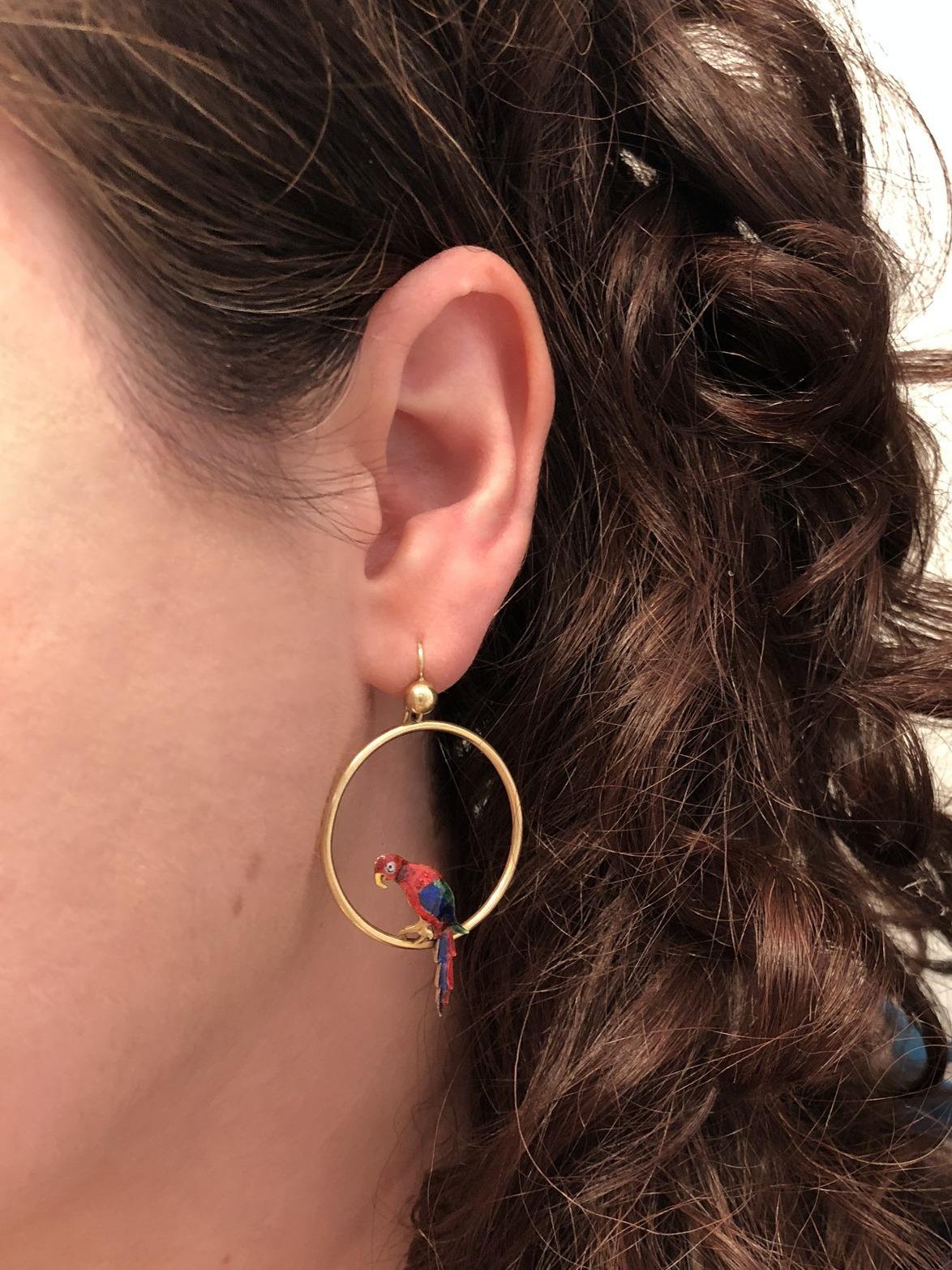 Whimsical bird earrings depict colorful parrots in red, blue and green enamel perched within delicate hoops of 15 karat yellow gold. Stamped 15K.  Fitted Box from Hamilton & Co. Length 2-1/8in, width 1-1/4in.