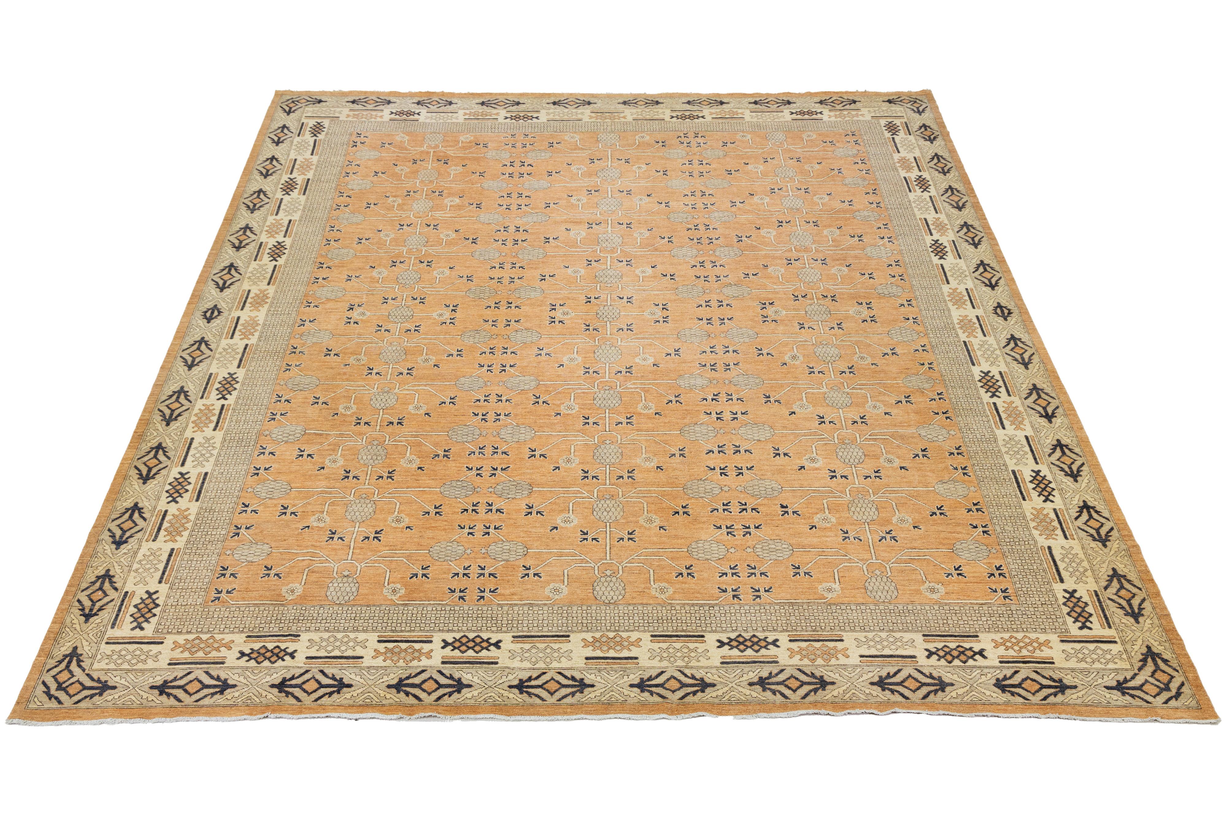 Ce tapis surdimensionné en laine nouée à la main, de style Khotan, présente un champ orange avec des accents bruns et beiges. Le design présente un motif all-over qui incorpore des éléments de style moderne.

Ce tapis mesure 15'1