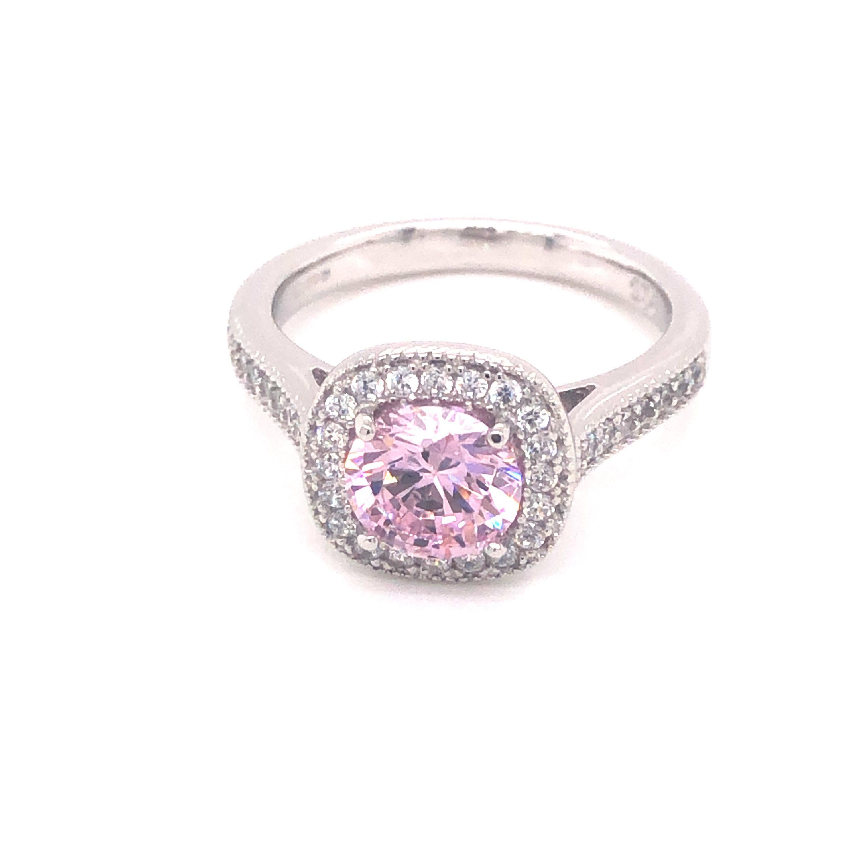 This classic halo style engagement ring is a breathtaking symbol of romance and elegance. At the center, there is a radiant 1.50 carat pink cubic zirconia, expertly cut to showcase its vibrant color and brilliance. Surrounding the pink stone is a