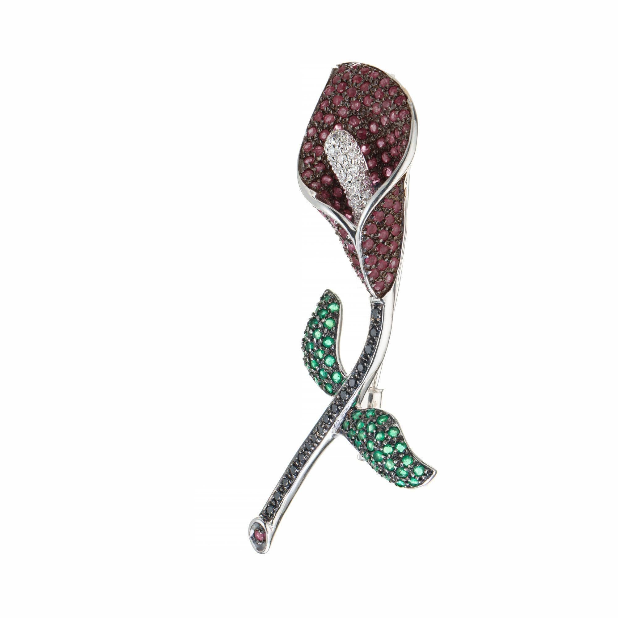 Three dimensional Calla lily pendant and brooch. 109 round red rubies and 29 round diamonds make up the lily with 43 round green emeralds making up the leaves. 16 round black diamonds finish off the stem. This beautiful brooch was created in 18