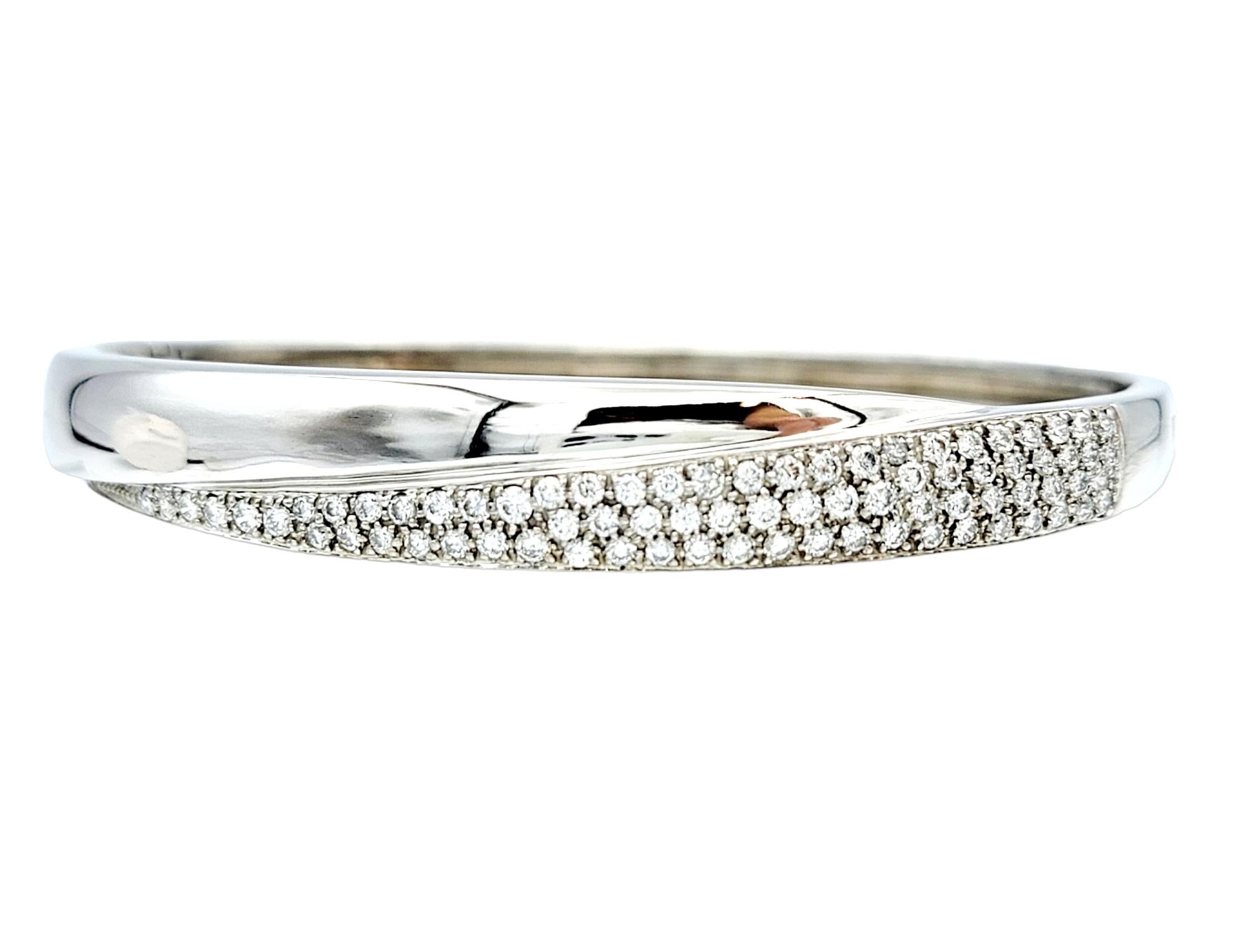 This hinged bangle bracelet, crafted in exquisite 14 karat white gold, embodies timeless elegance. Its design features a captivating and harmonious overlapping or layered design. The first layer is adorned with a stunning array of pave diamonds,