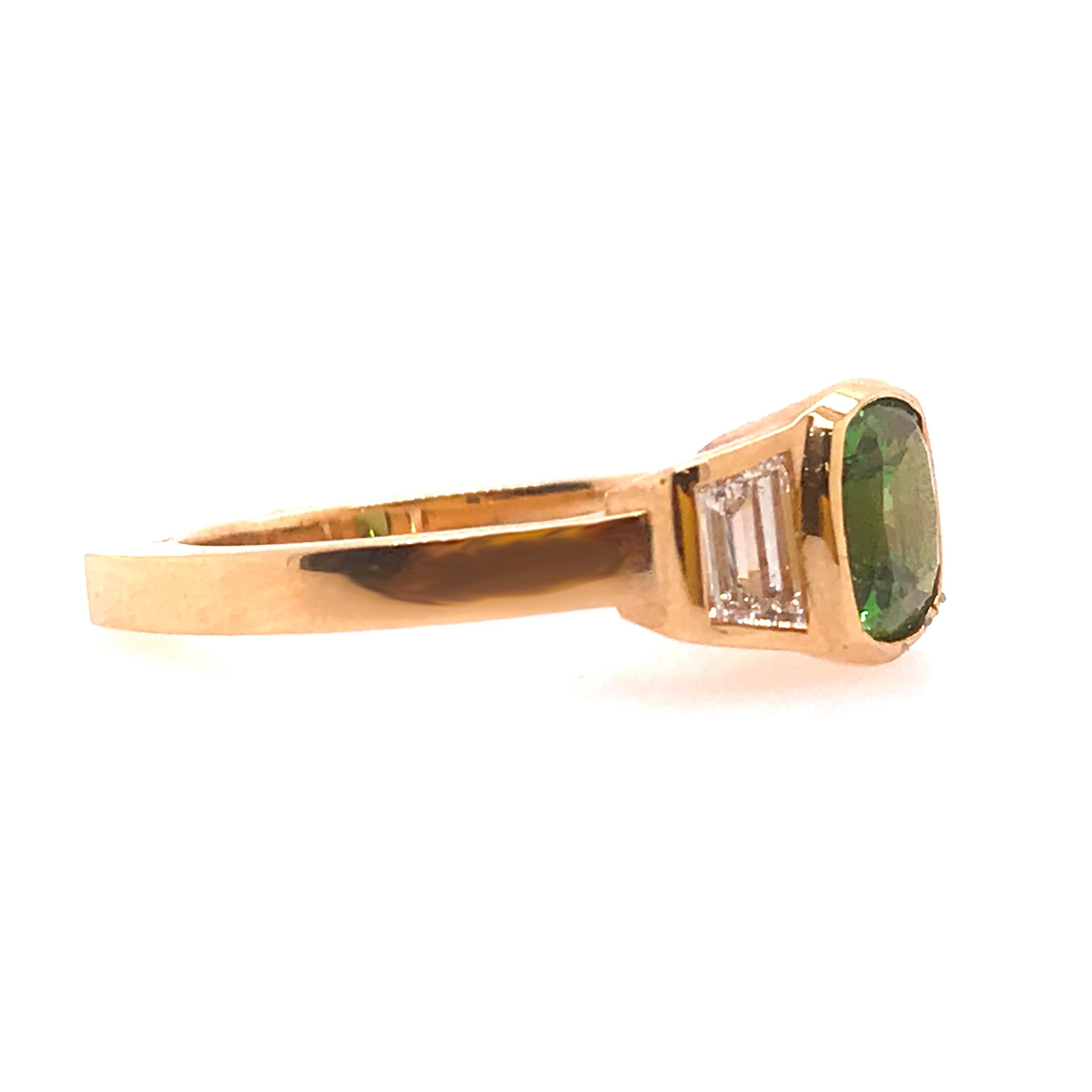 A custom one of a kind three stone ring with a cushion shape tsavorite garnet set in a modern yellow gold bezel. The center is flanked by two trapezoid shaped diamonds. The side diamonds are set in yellow gold bezels. The design is very clean and