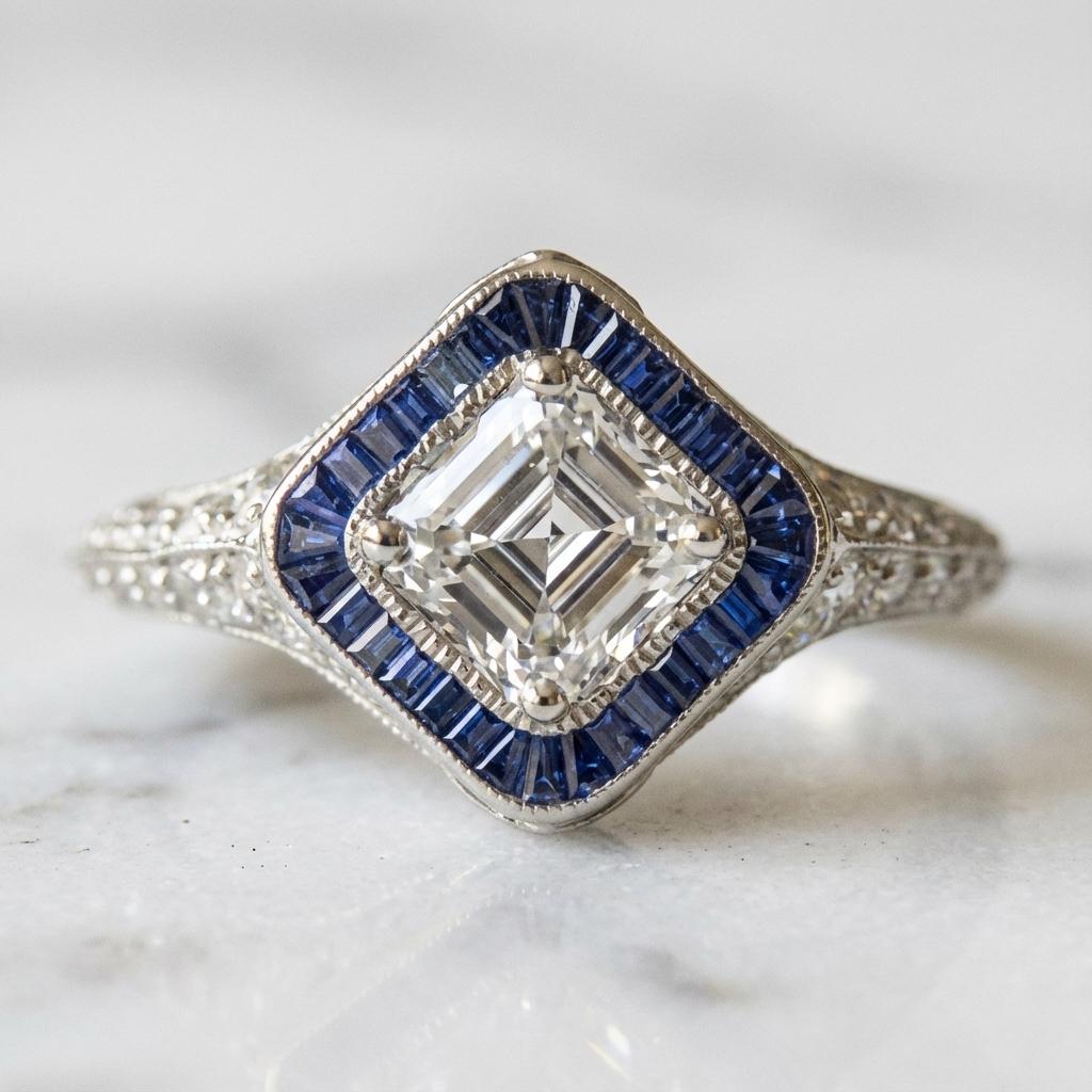 Cette bague de style vintage associe un diamant de taille Asscher certifié par la GIA à des saphirs naturels aux teintes riches, sertis dans de l'or blanc poli 14k. 

Le poids total en carats est d'environ 1,50 ct, les facettes géométriques du