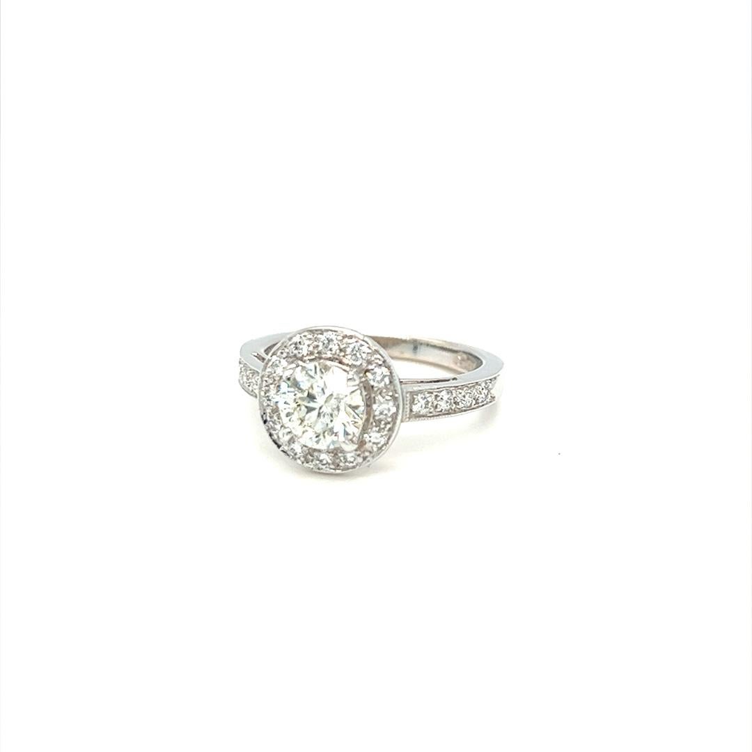 Classic halo engagement ring with 0.90 carat G color and SI clarity round brilliant cut diamond. The ring is crafted in 18K white gold with beautiful bead work detail with small diamonds weighing approximately 0.60 carat in total. Currently in size