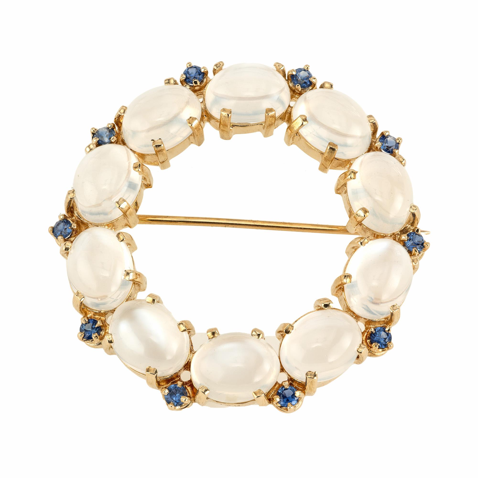 Umfassen Sie die zeitlose Eleganz der 1960er Jahre mit unserer exquisiten 15,00ct Mondstein und Saphir Kreis Brosche. Dieses meisterhafte Stück ist eine Harmonie aus Kunst und Natur, in der der leuchtende Mondstein die Hauptrolle spielt. Besetzt mit