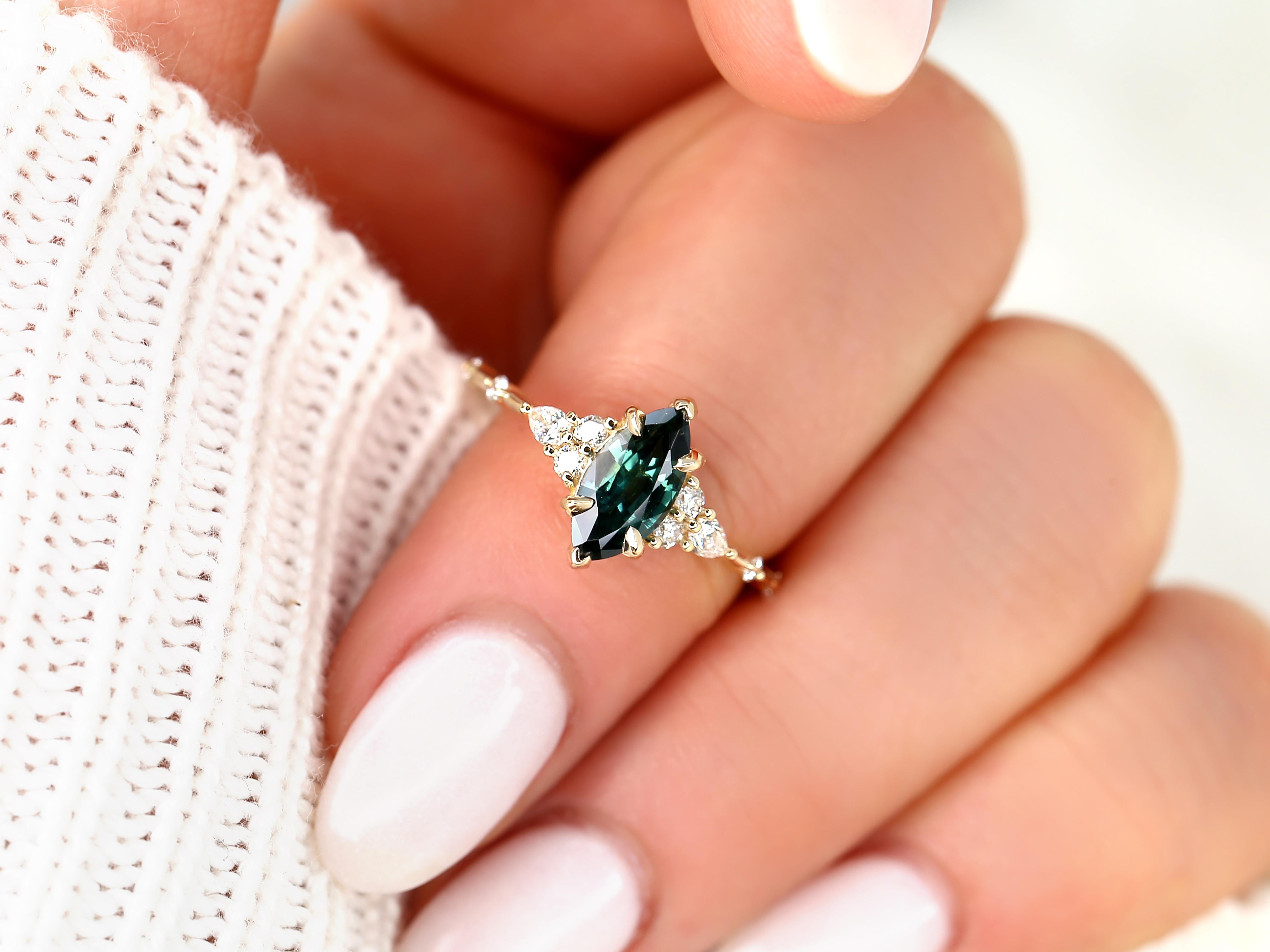 Explore our exquisite marquise teal sapphire cluster ring Astrid, featuring a stunning teal sapphire set in a dainty yet sophisticated 14kt gold design, accented with natural diamonds. Discover timeless elegance in every detail.

Details of
