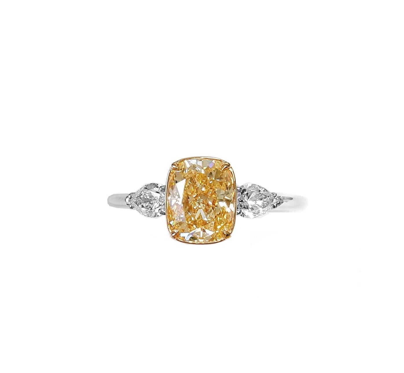 This stunning engagement ring showcases a 1.50 carat natural fancy yellow-orange cushion cut diamond as its centerpiece, GIA certified with SI2 clarity. The vibrant yellow-orange hue of the diamond is beautifully complemented by two pear cut white