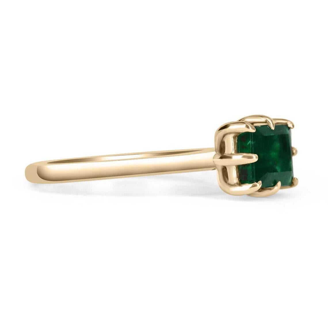 Displayed is an East to West DARK rare emerald solitaire emerald-cut engagement ring/right-hand ring in 14K yellow gold. This gorgeous solitaire ring carries a full 1.50-carat emerald in an eight-prong setting. Fully faceted, this gemstone showcases