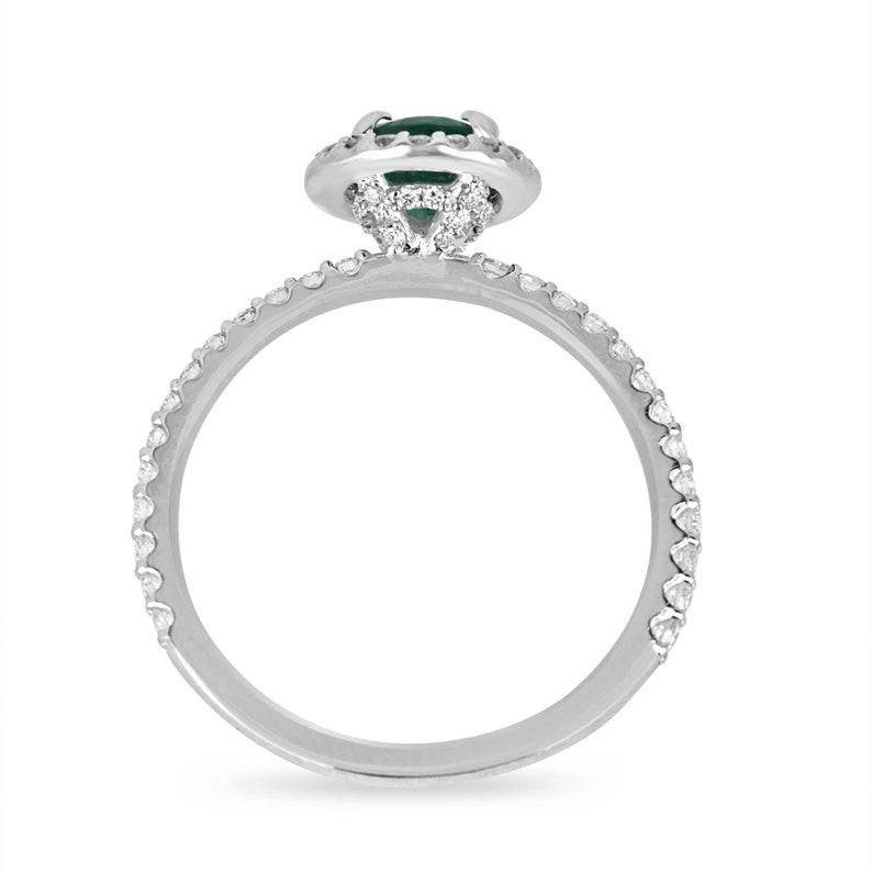 Experience enchantment with our Emerald and Diamond Halo Engagement Ring, showcasing a captivating 1-carat Zambian oval emerald at its heart. Its medium lush green hue, semi-transparent clarity, and very good luster exude natural charm, set in a