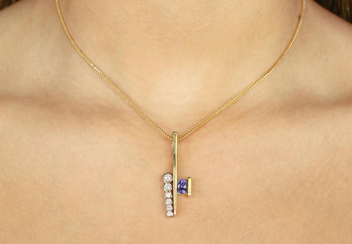 An unusual tanzanite and diamond gold pendant. A fancy tanzanite oval is suspended in an exquisite yellow gold channel set and is the center of attention. The gem exalts a vivacious, dark lavender color with excellent clarity. Off setting the