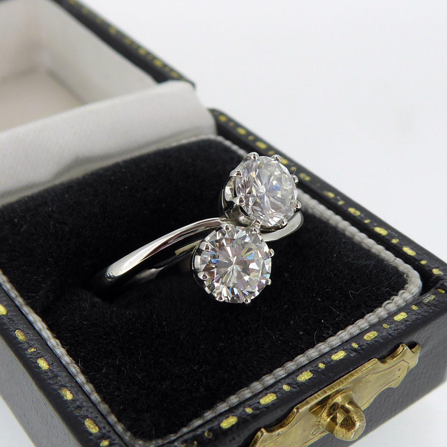 A previously owned diamond ring set with two round brilliant cut diamonds in claw mounts to a cross over style ring.  One diamond measures approx. 5.83mm x 5.88m x 3.42mm deep, weighing 0.77ct and with clarity and colour assessed as SI and H/I.  One