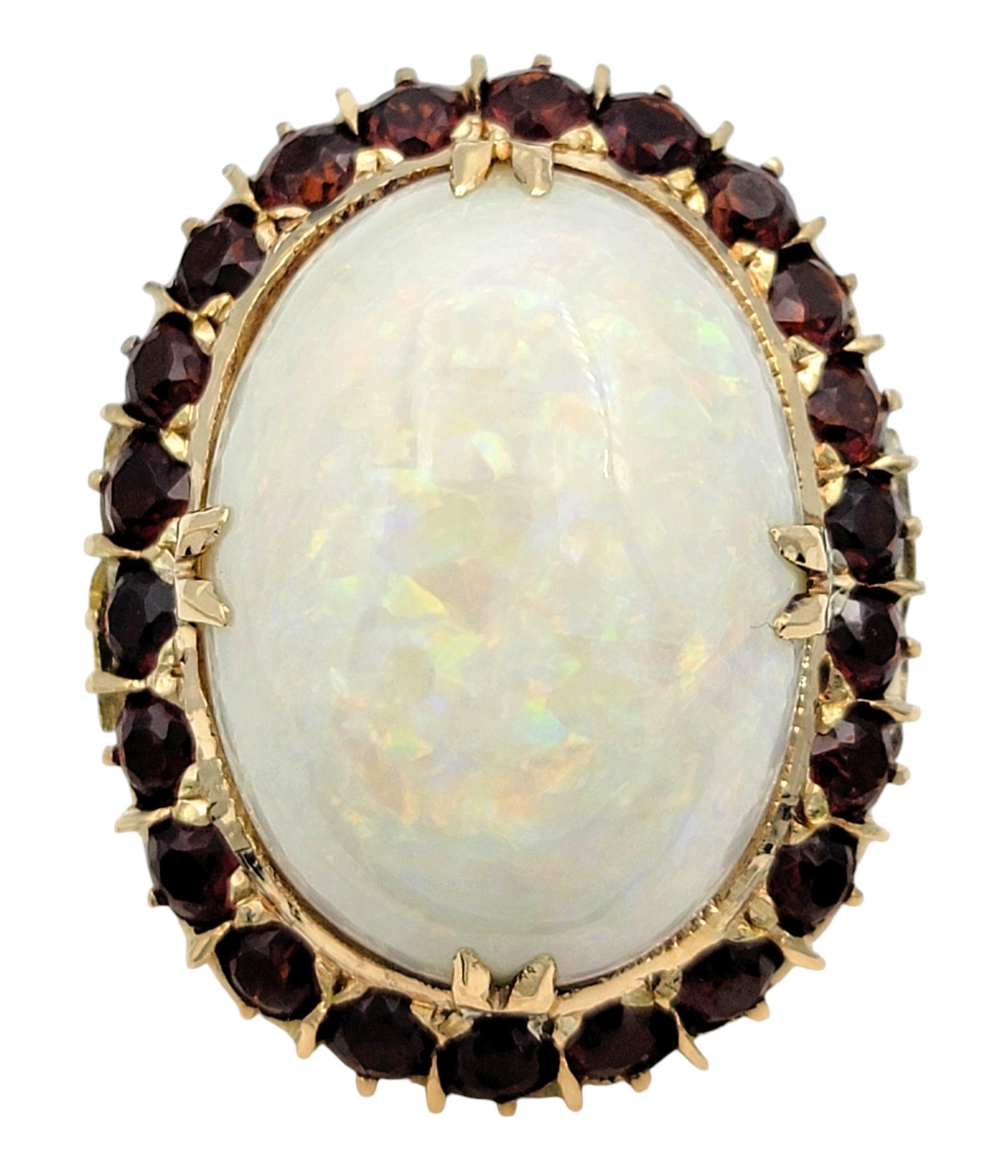 Ring Size: 6.5

A mesmerizing blend of color and brilliance, this exquisite ring features an oval cabochon-cut opal that shimmers with a captivating play of multiple colors. The opal’s ethereal glow is beautifully framed by a halo of rich red