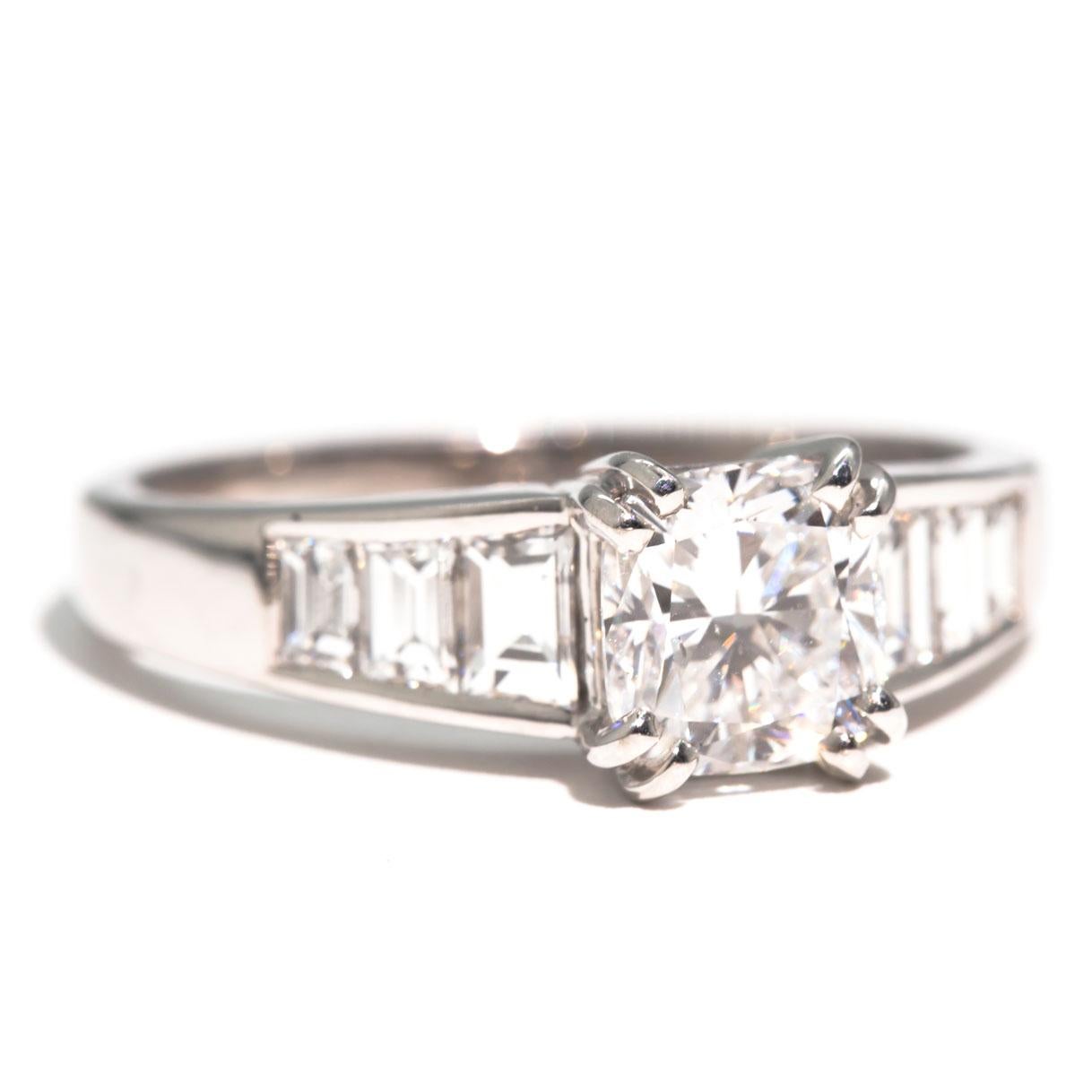 Crafted in 18 carat white gold is this breathtaking diamond engagement ring featuring a wondrous 1.52 Carat GIA certified cushion cut diamond flanked with bright white trapezoid diamonds in the band. We have named this stunning vintage ring The