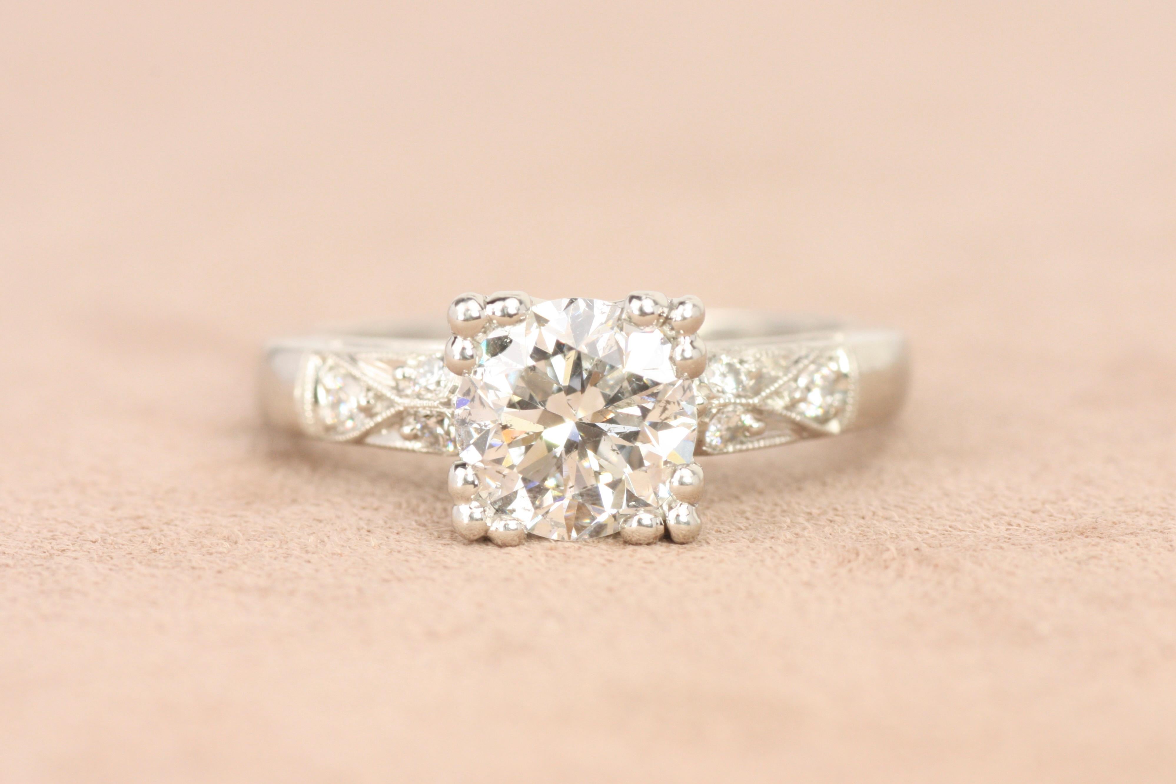 This vintage-inspired platinum engagement ring showcases a 1.42ct round diamond in a square fishtail setting, accented by intricate milgrain details and six side diamonds. The 1950s aesthetic combines classic beauty with a touch of added flair,