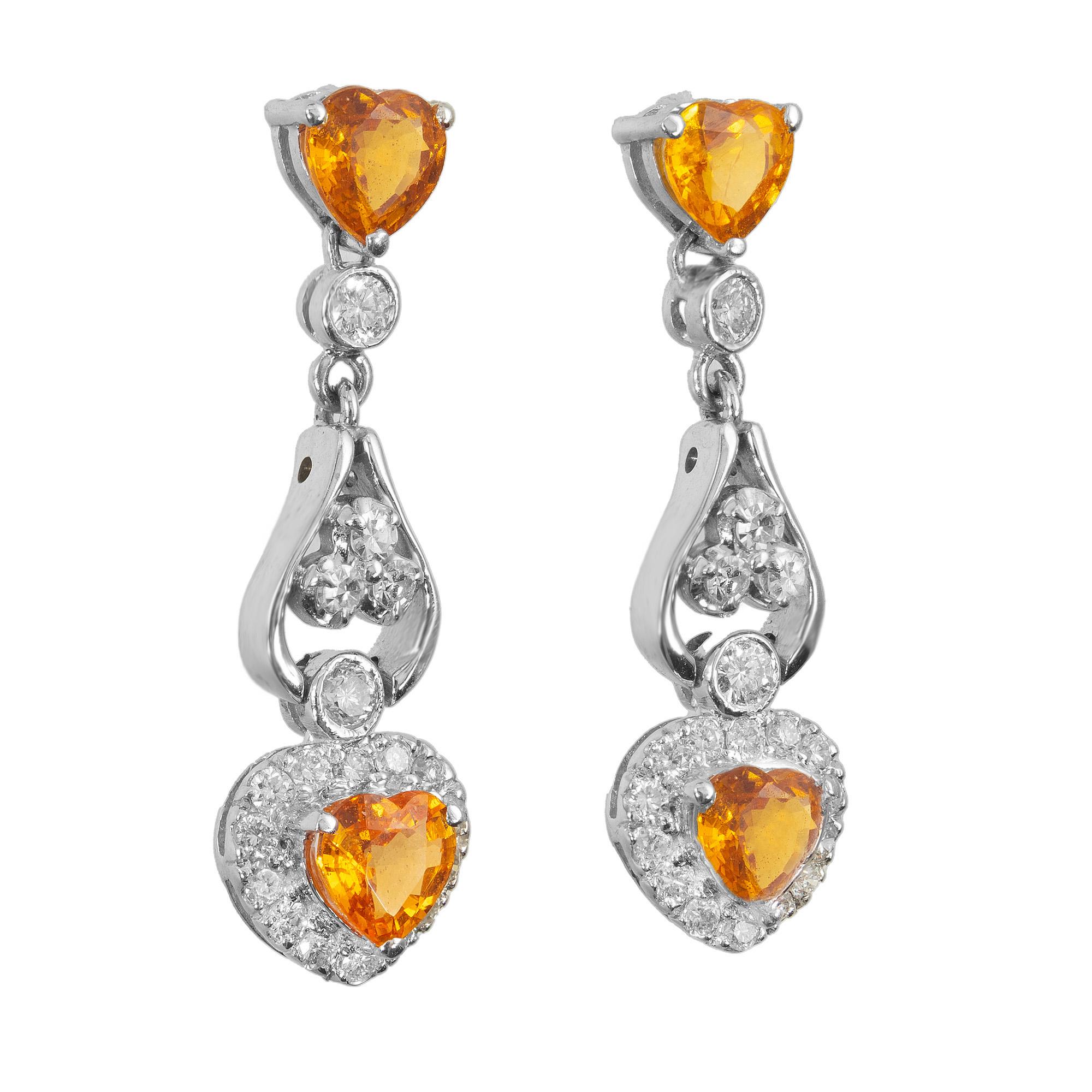 Orecchini pendenti in oro bianco 14k con zaffiri gialli a forma di cuore e aureola di diamanti. Gli zaffiri a forma di cuore sono di un giallo brillante e non presentano segni di trattamenti termici, mentre i diamanti circostanti sono bianchi,