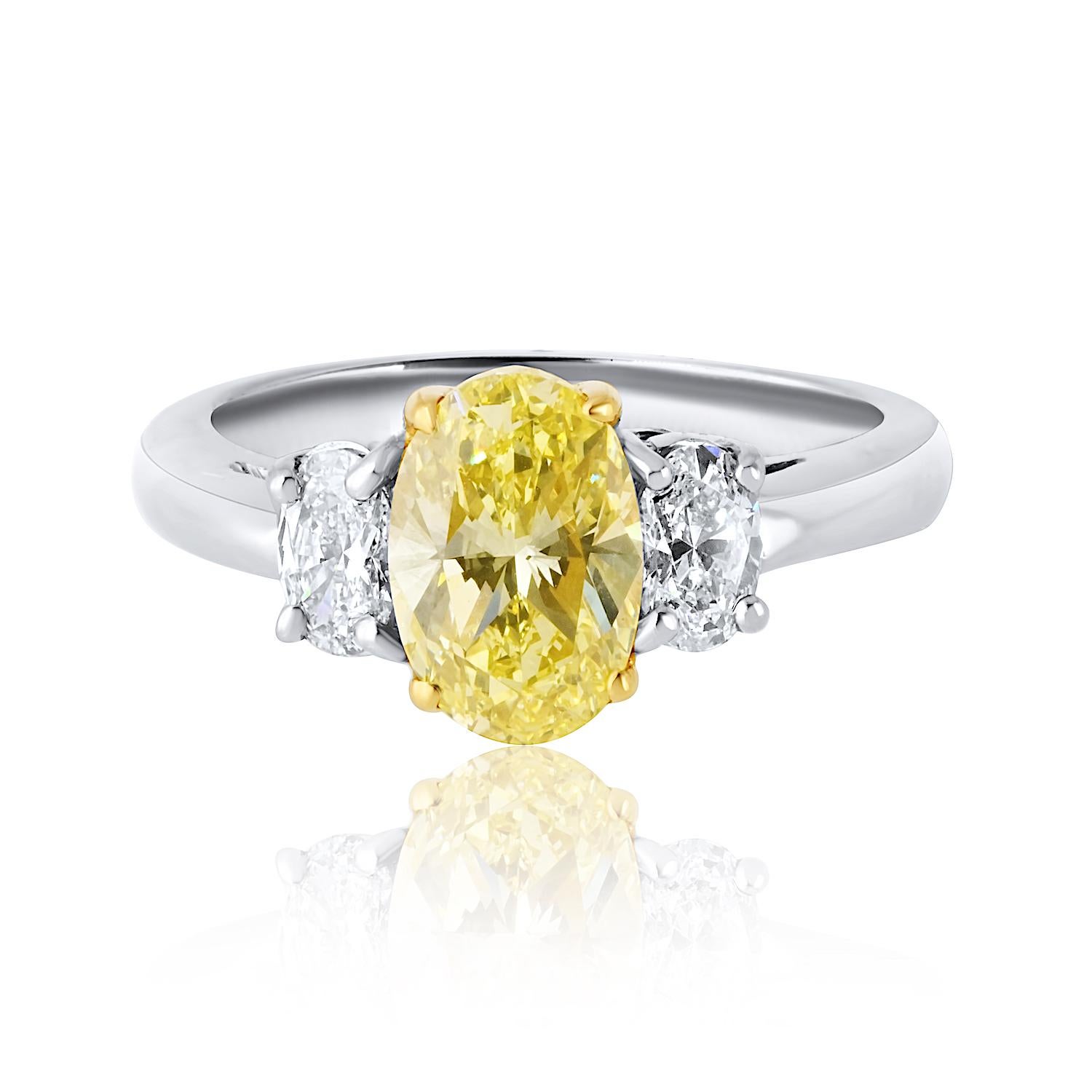 This stunning three-stone engagement ring features a vibrant 1.54-carat oval cut diamond with a mesmerizing Fancy Intense Yellow hue, GIA certified for its exceptional color and brilliance. Accentuating the center stone are two perfectly matched