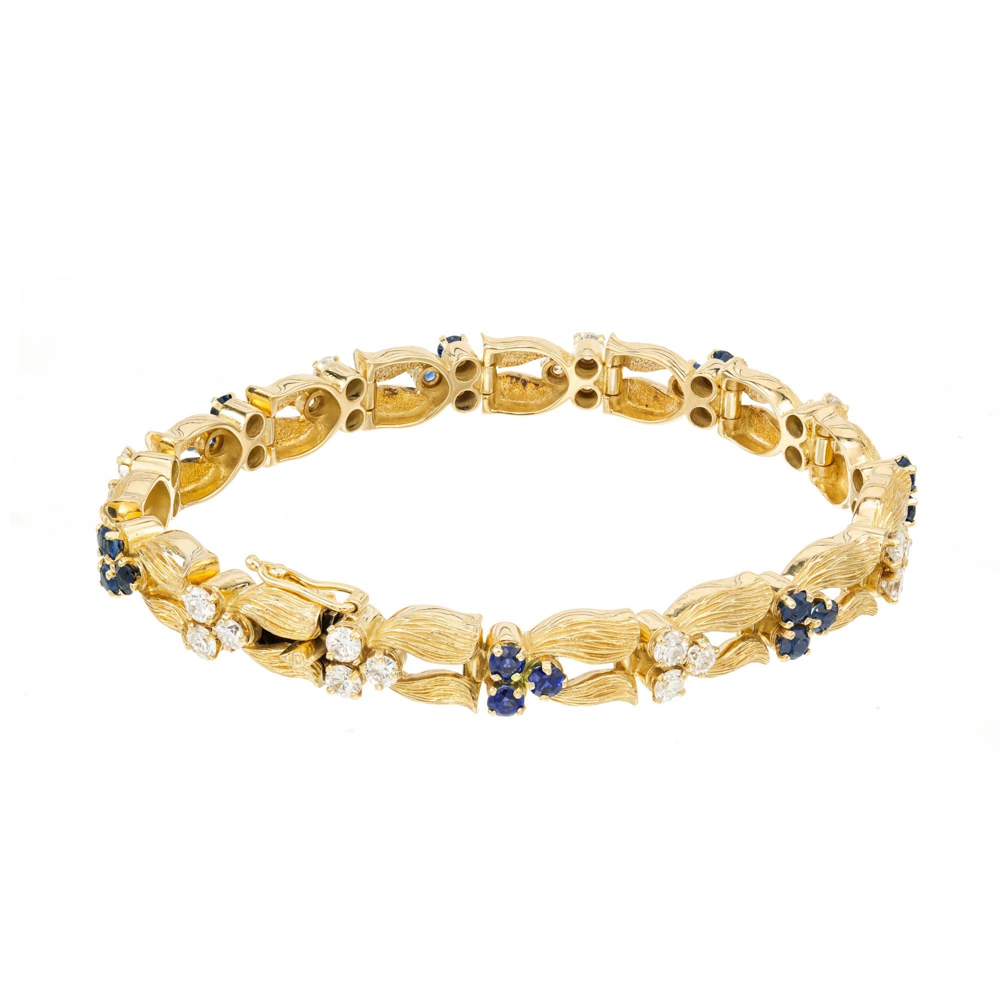 1970's Wonderful sapphire and diamond style flower design hinged link bracelet. Swiss crafted, this 18k yellow gold textured bracelet is adorned with clusters of 3 round diamonds and 3 round sapphires in a flower petal design. Excellent condition