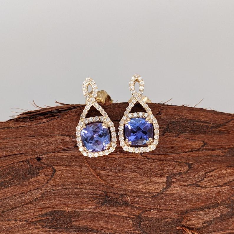 These gorgeous cushion cut Tanzanites are stunning in this pair of earrings, accentuated by the setting in 14k solid yellow Gold and natural diamond accents. Tanzanites have a beautiful blue color with flashes of red and purple. The Tanzanites are