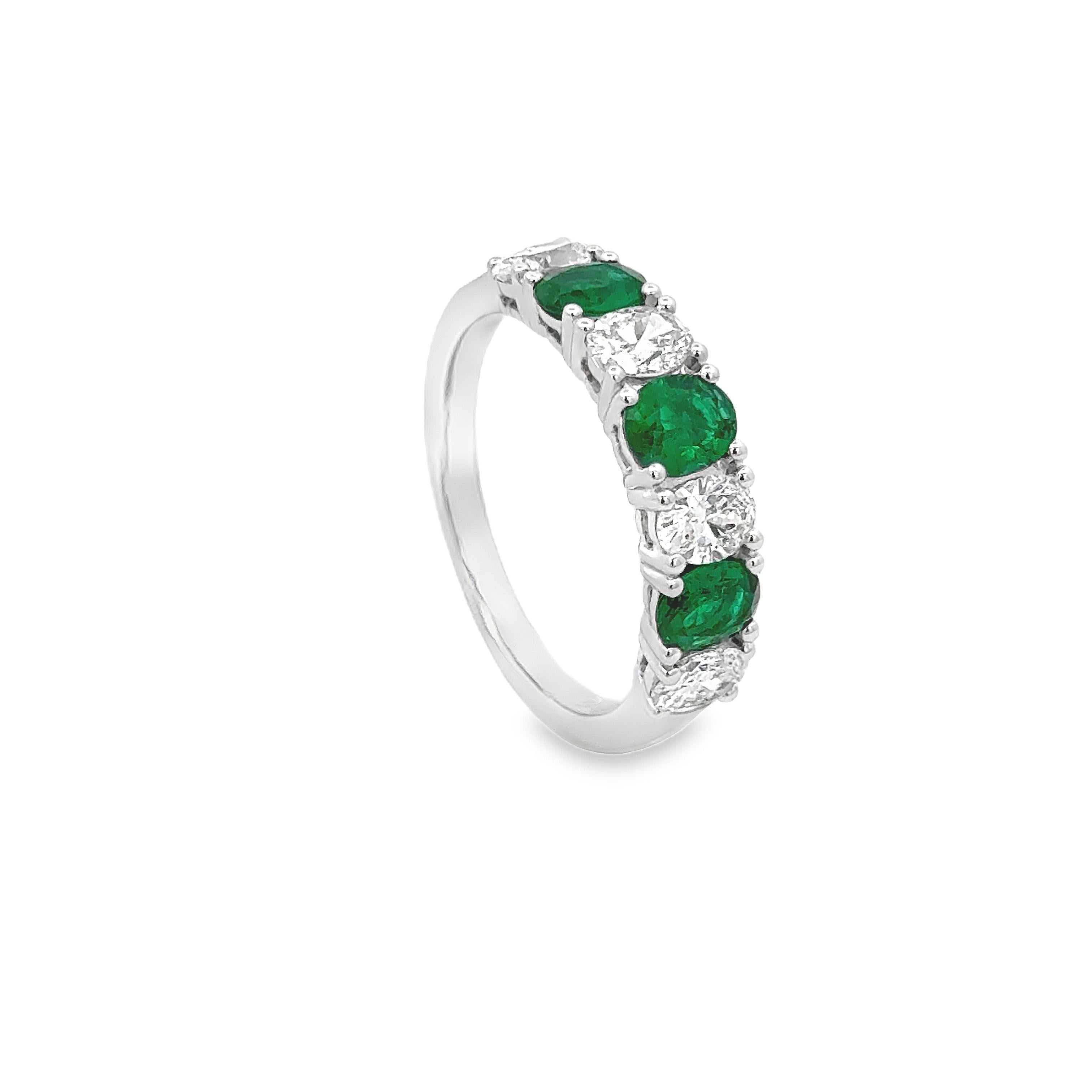 A beautiful wedding band ring, showcasing four oval brilliant cut diamonds weighing 0.84 carat total and three oval cut emeralds weighing 0.72 carat total, each set on a four prong setting in an alternating fashion. Finely made with 18K white gold.