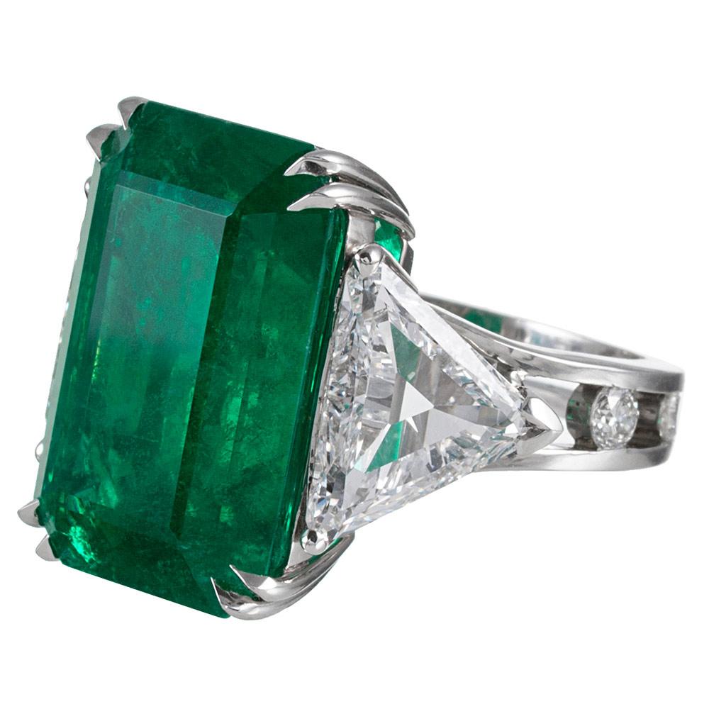 An outstanding adornment for the fine jewelry enthusiast, displaying an impressive emerald center stone flanked by a pair of trillion cut white diamonds. The major stone exhibits saturated, intense true emerald green color and is of remarkable