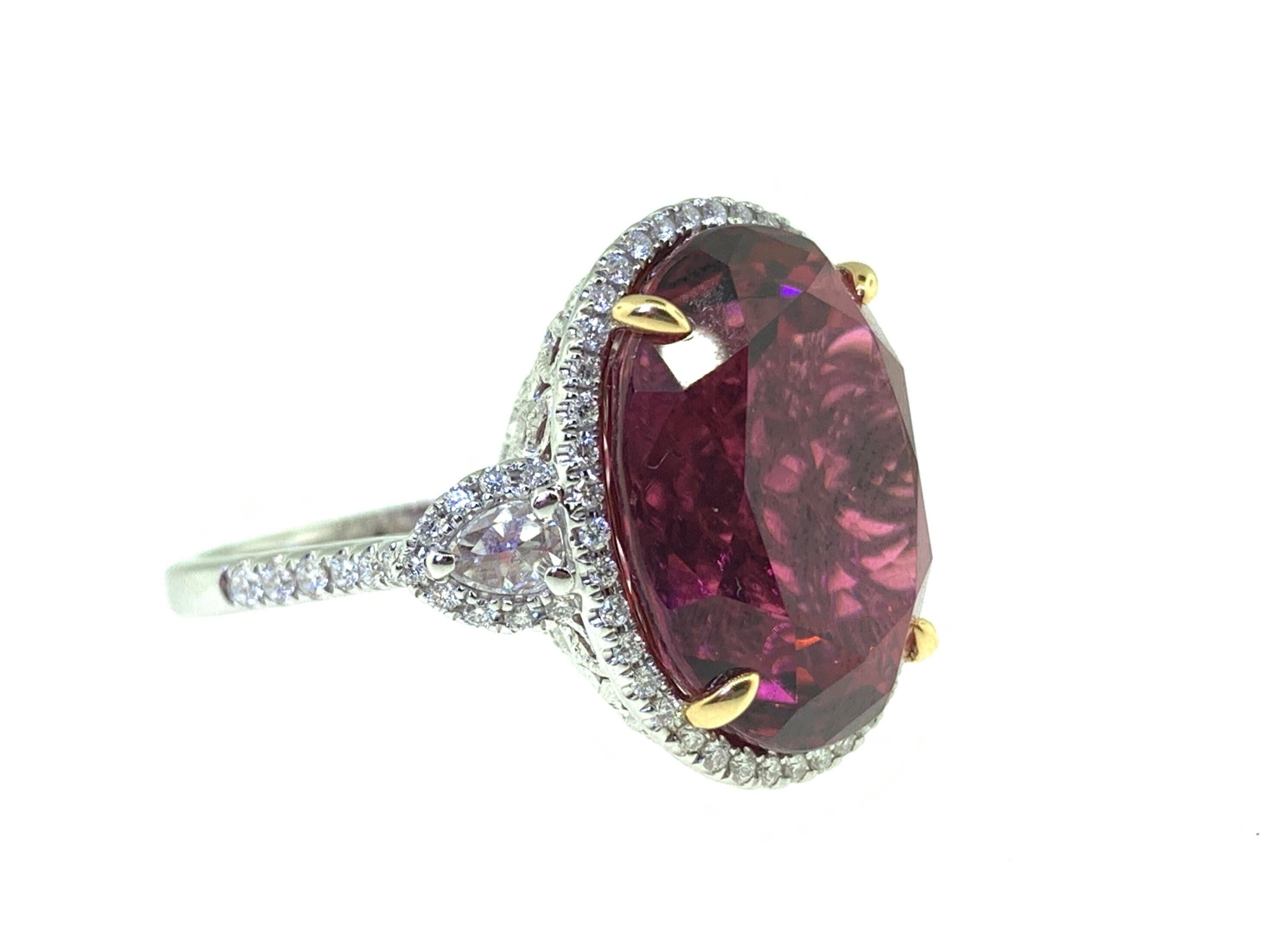 This stunning cocktail ring showcases a large 15.65 Carat Oval Rubellite Tourmaline with a Diamond Halo. The Rubellite is flanked by two Rose Cut White Diamonds and is set in 18k white gold, with 18k yellow gold prongs on the center stone. Total