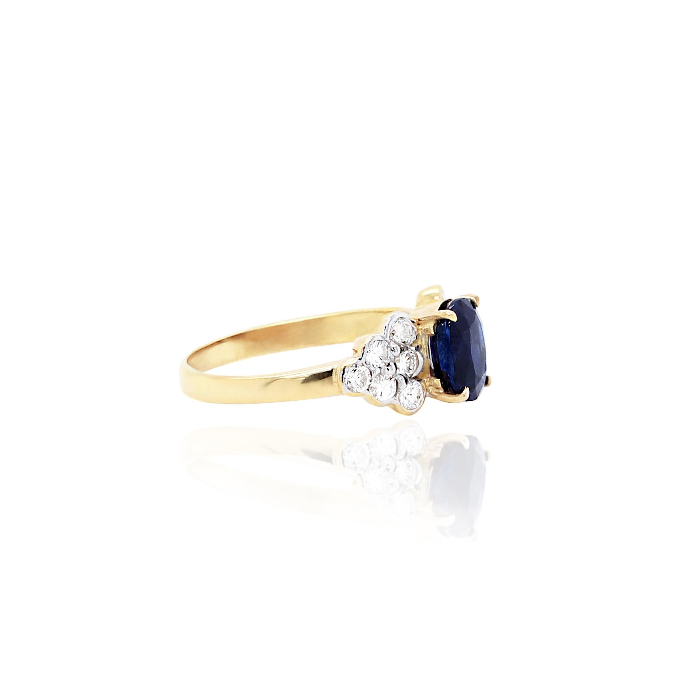 This beautiful engagement ring features a royal blue oval sapphire weighing 1.56ct mounted in a four claw open back setting. This lovely stone is accompanied by a cluster of six fine quality round brilliant cut diamonds on either side, totalling to